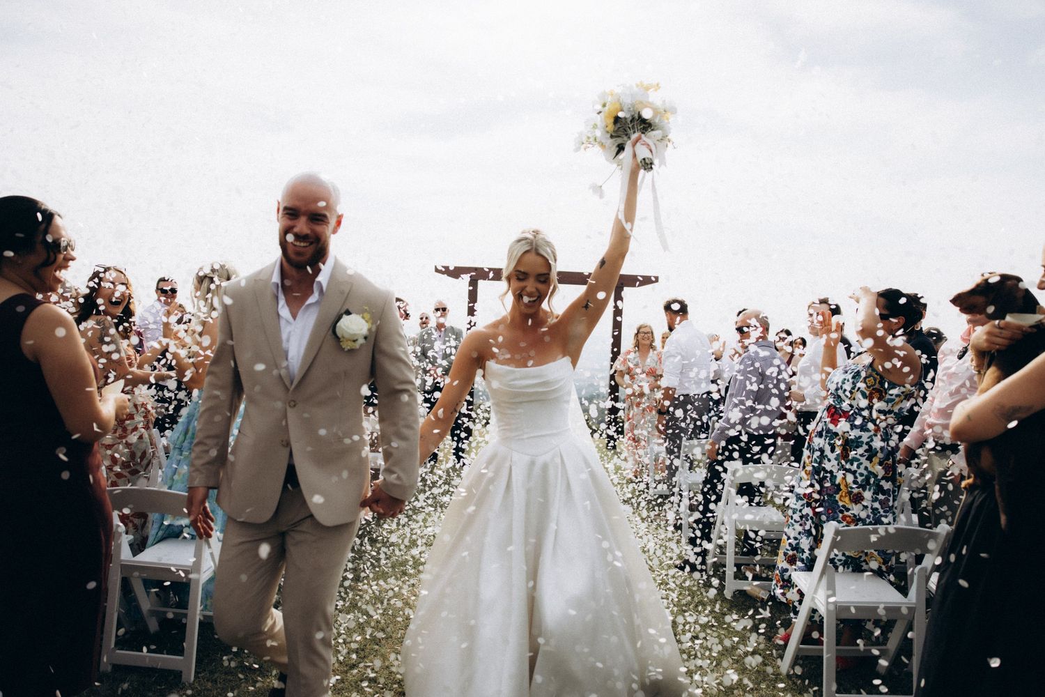 Joyful wedding celebration with confetti flying in the air during outdoor ceremony.