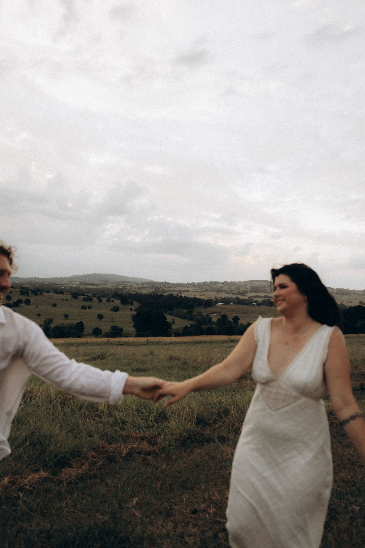 Couple in white clothing dancing together in a rustic outdoor setting.