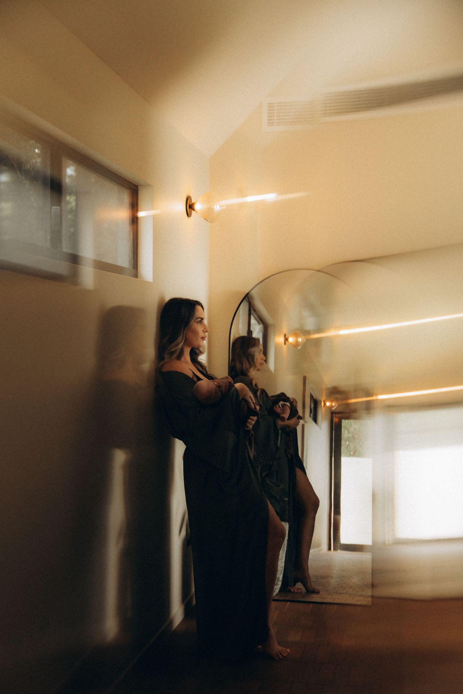 Person standing in a warmly lit interior space with dramatic shadows and reflections.