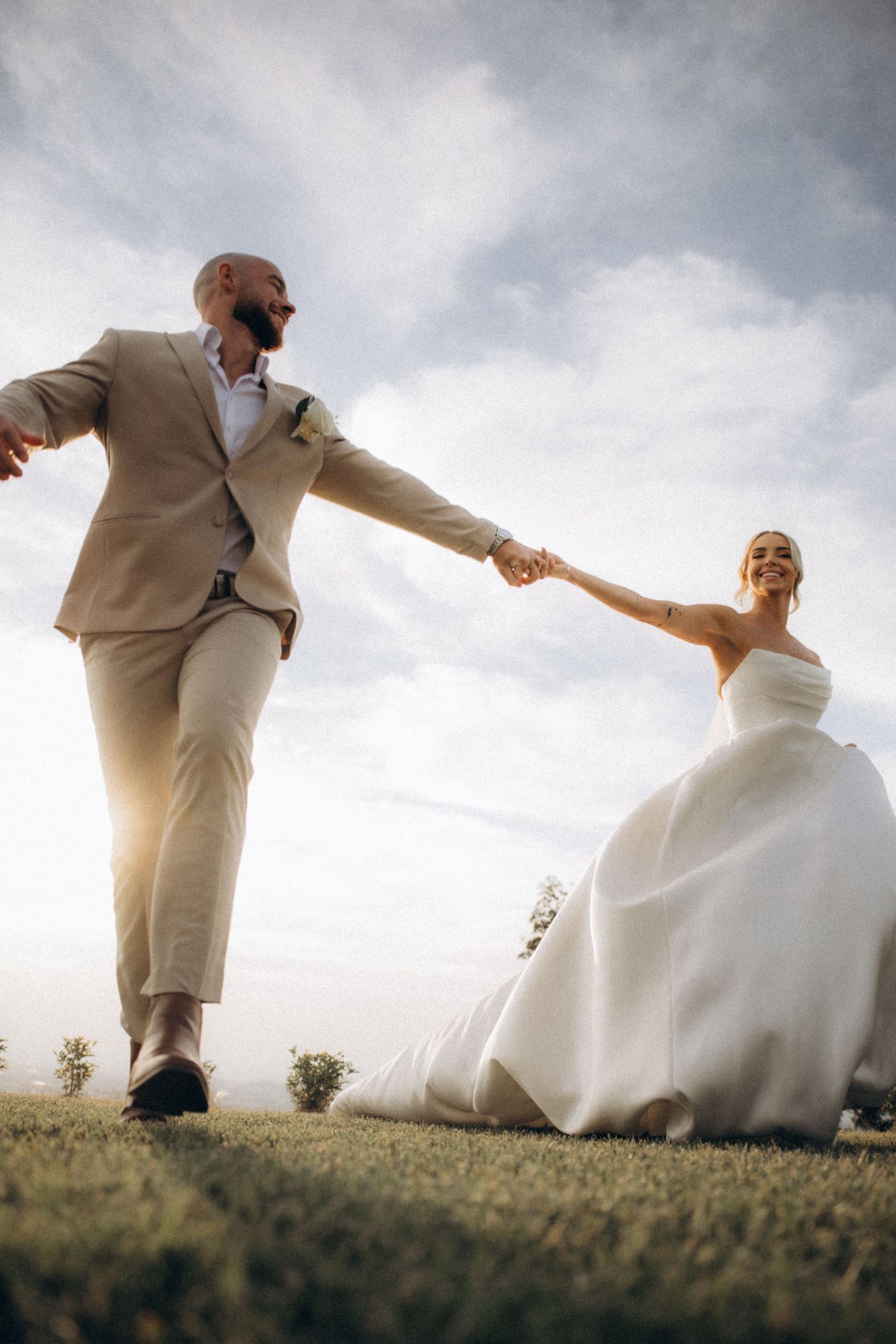 A playful dancing sequence of a couple in wedding attire on a grassy hill.