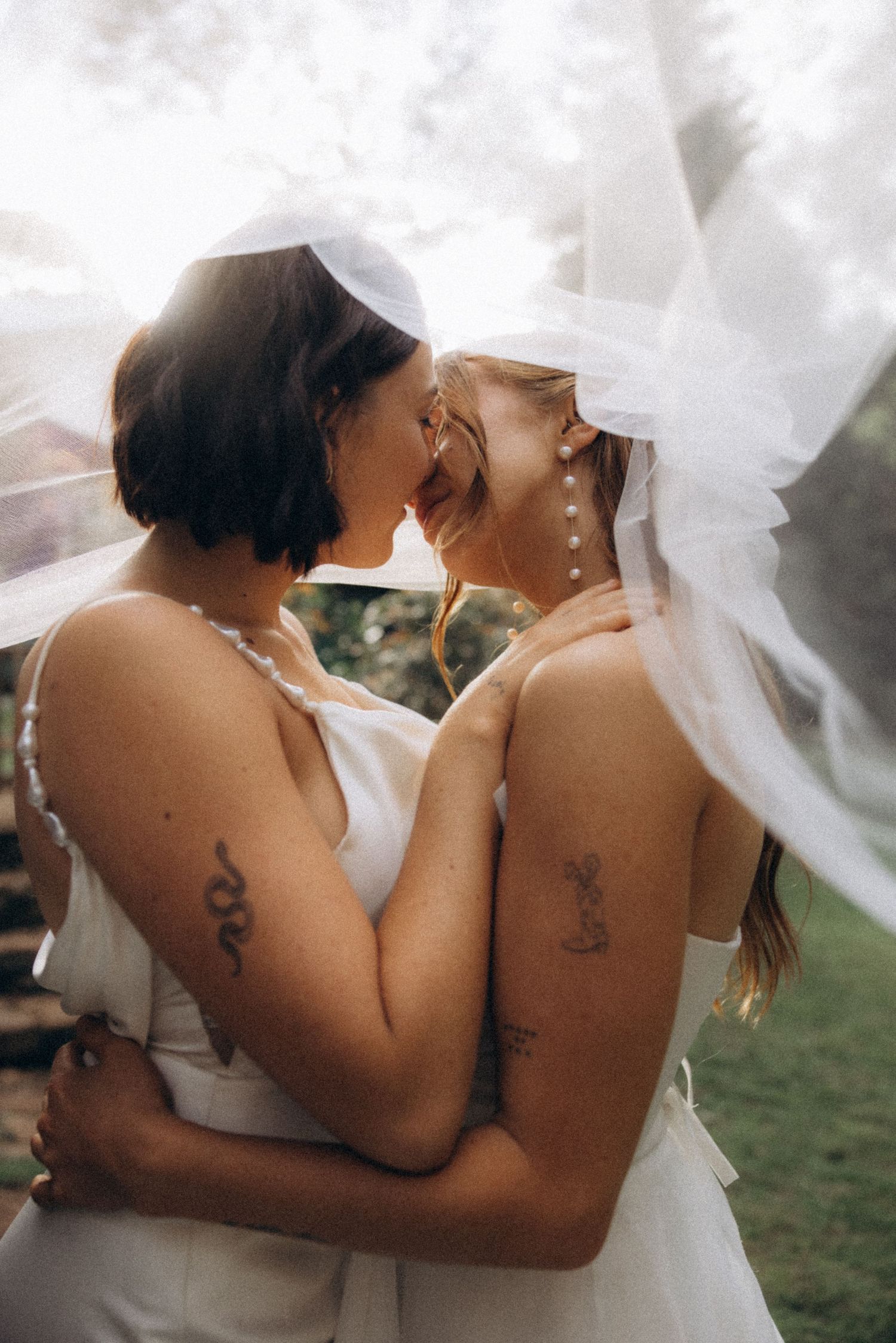 Close-up of matching tattoos on couple's backs with flowing white veil.