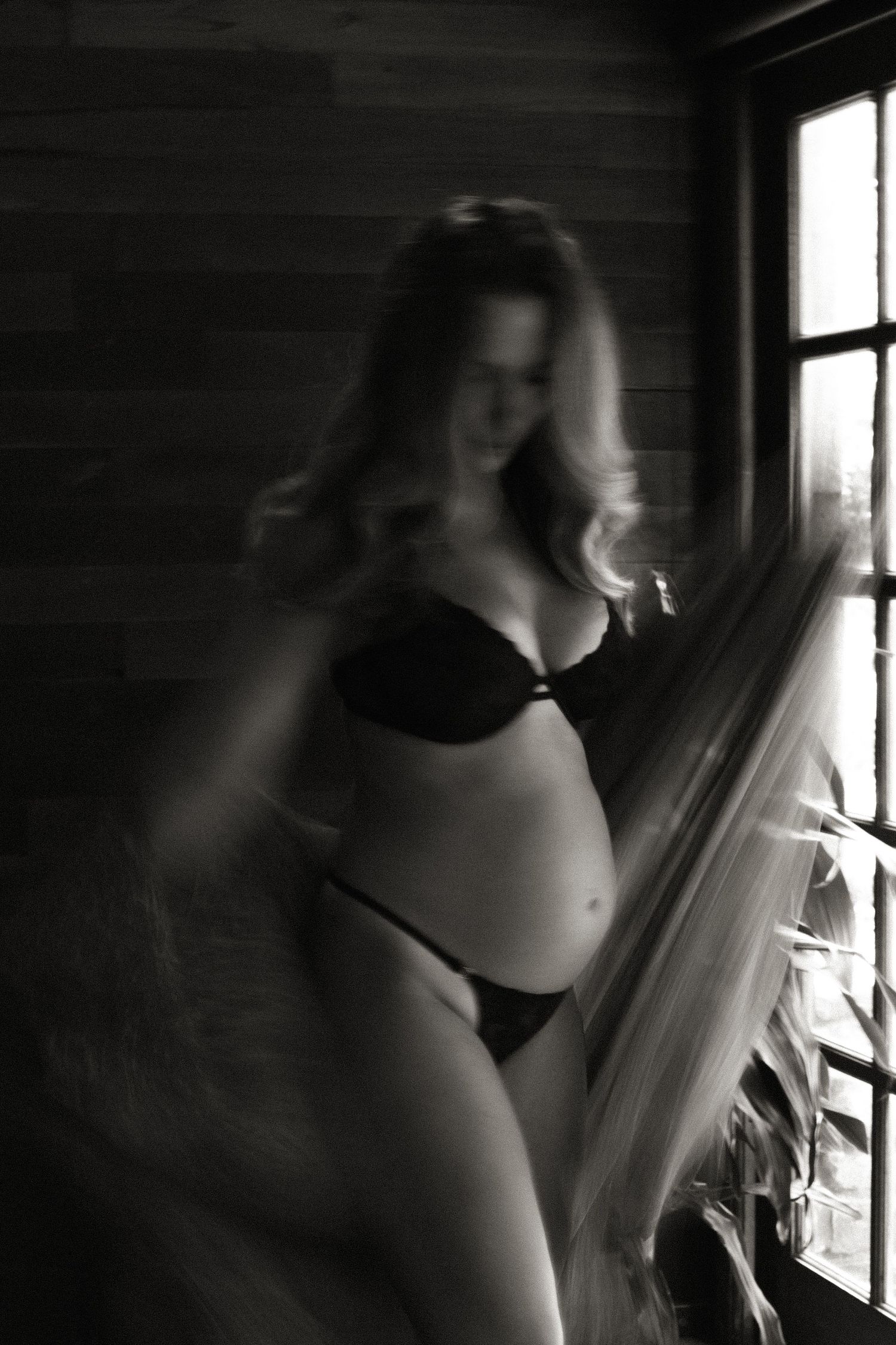 Artistic black and white photograph of a figure silhouetted against bright window light creating a dramatic mood.