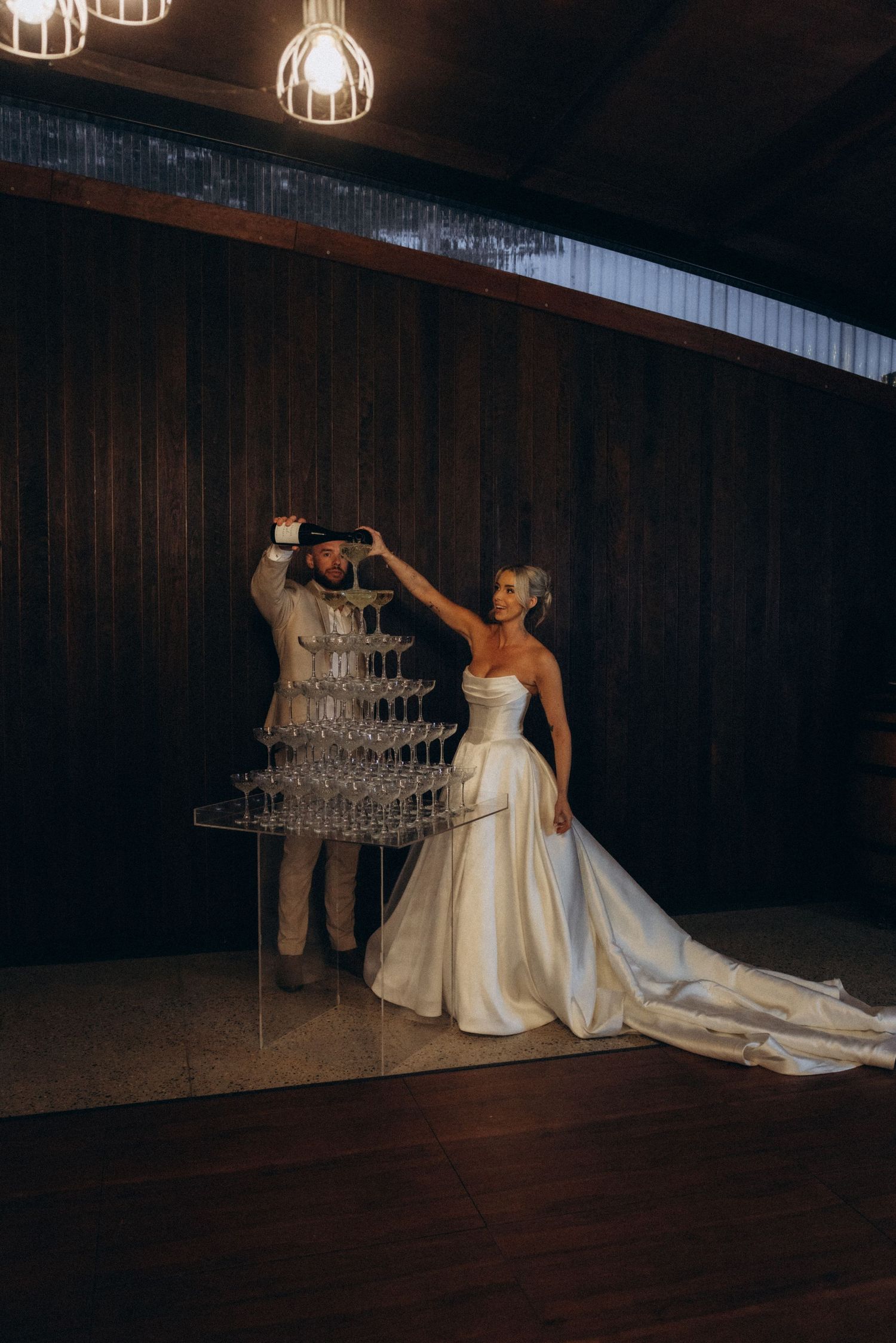 A couple poses dramatically with a champagne tower in an elegant venue.