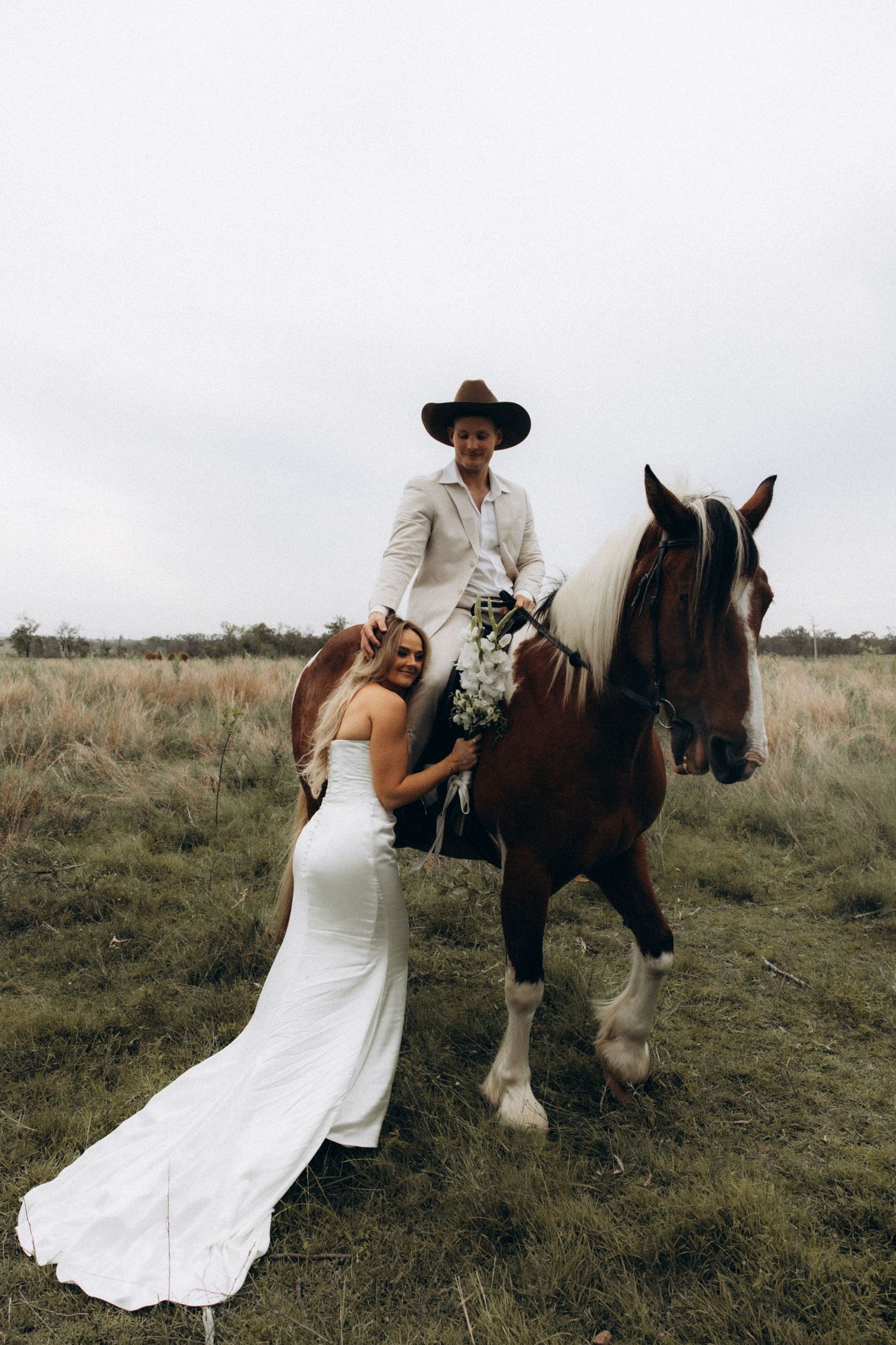 Wedding couple poses with a majestic draft horse in a grassy meadow.