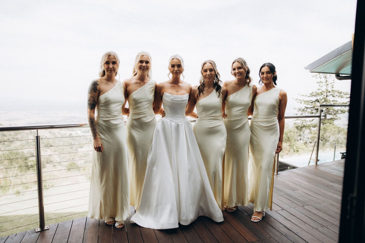 Bridesmaids in cream-colored dresses posing together on outdoor deck.