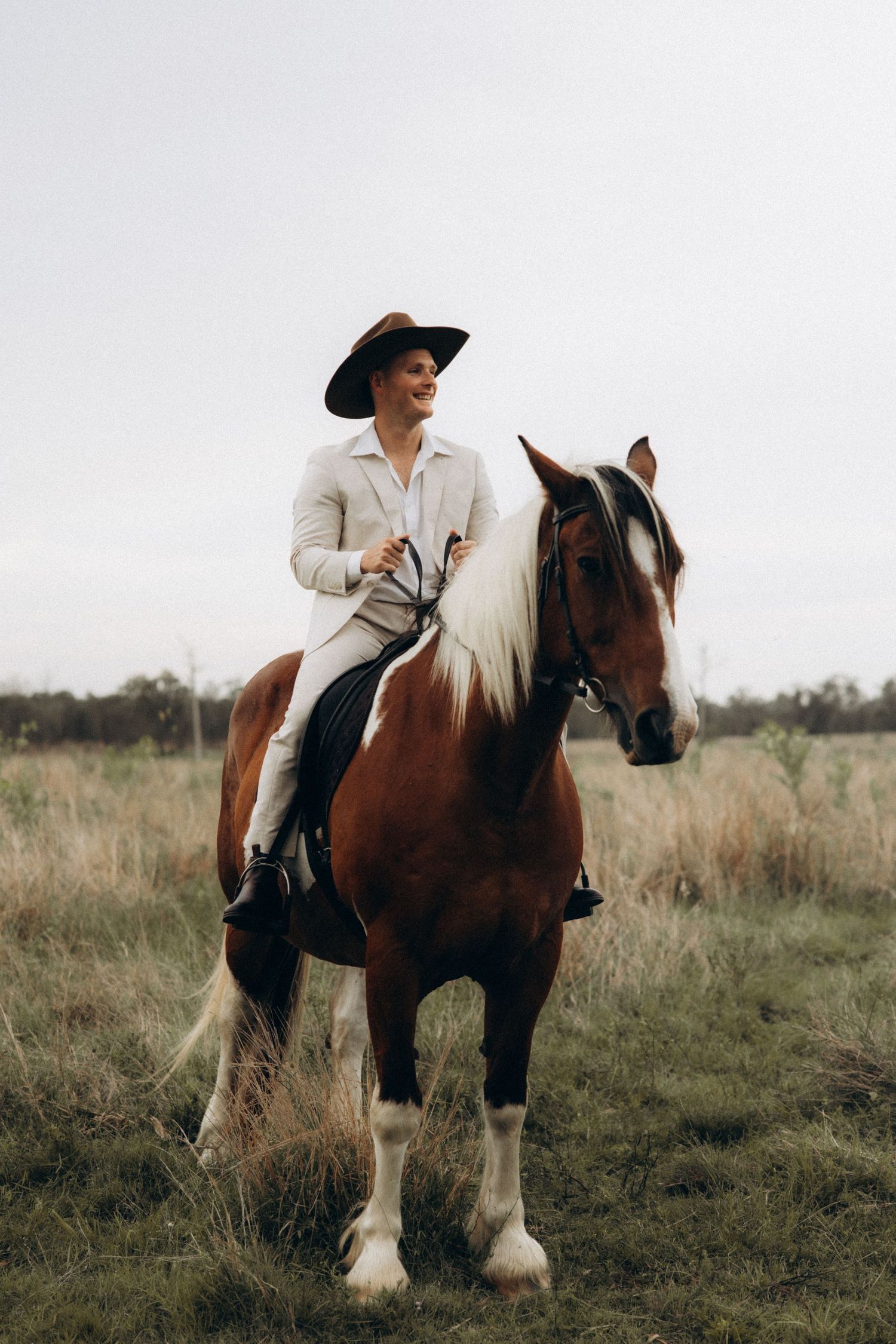 A couple poses with their draft horses in a serene countryside setting.