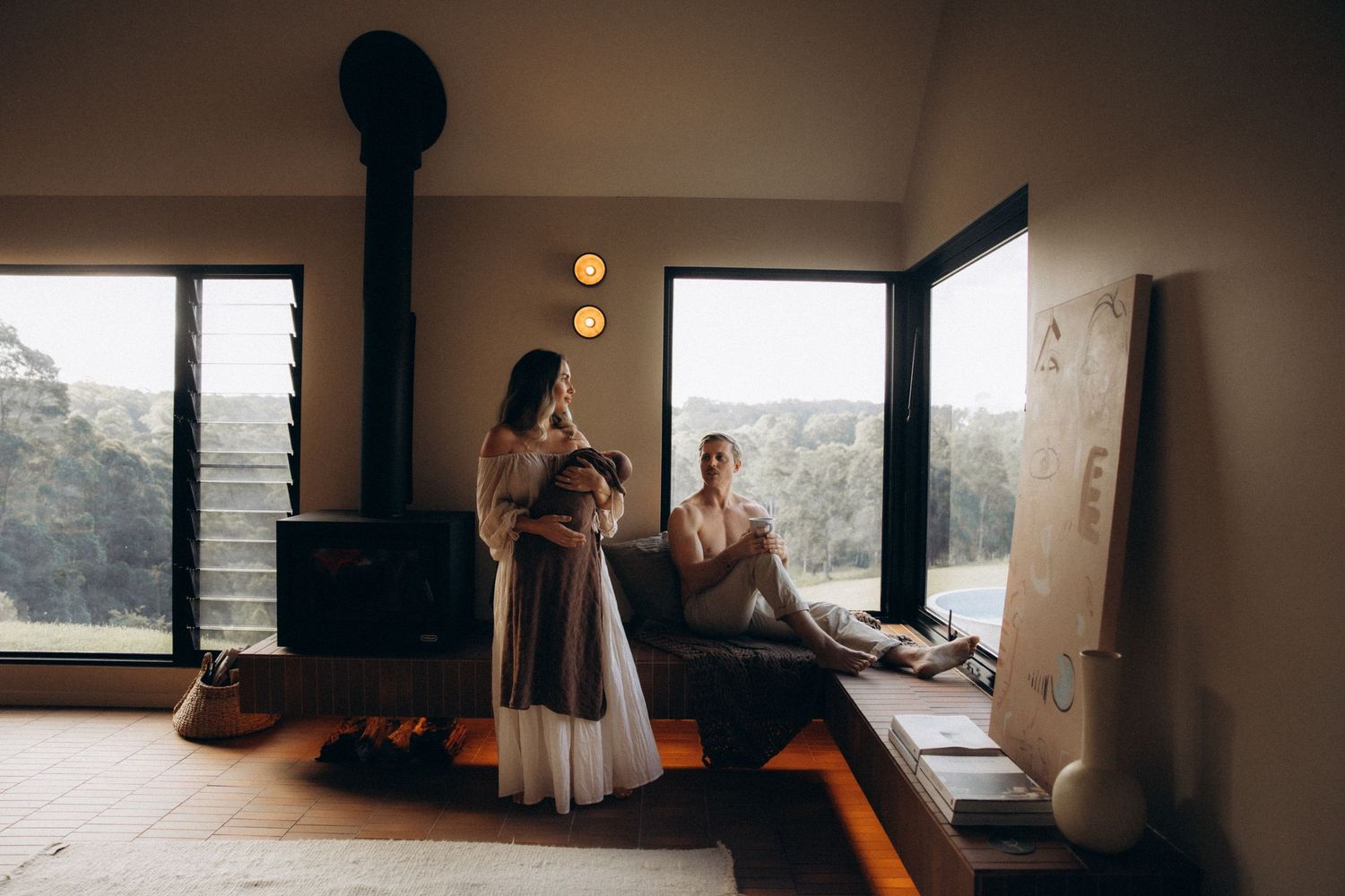 Family shares intimate moment near window in modern room with wood stove.