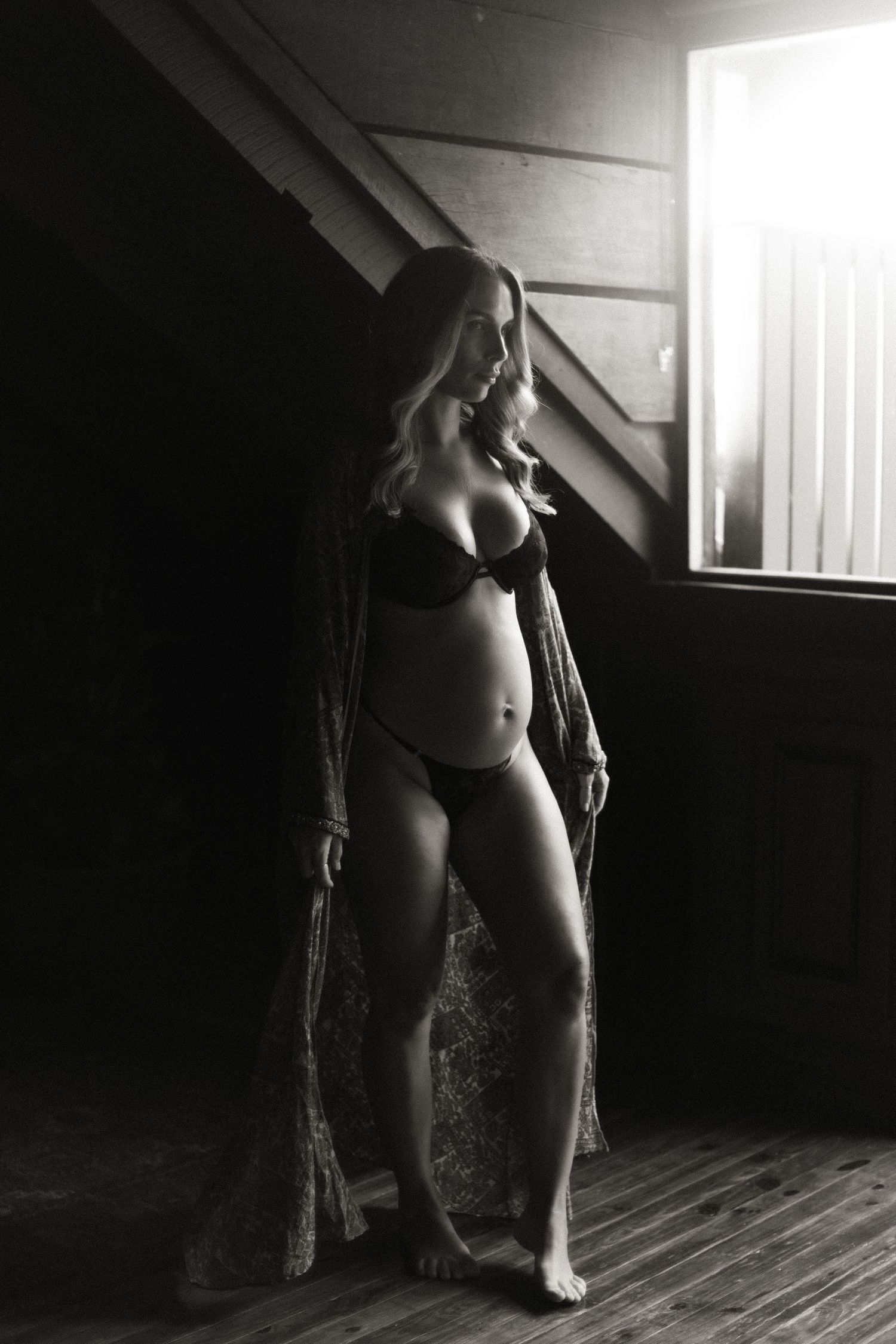 Dramatic black and white boudoir photos show silhouette against window light on wooden floor.