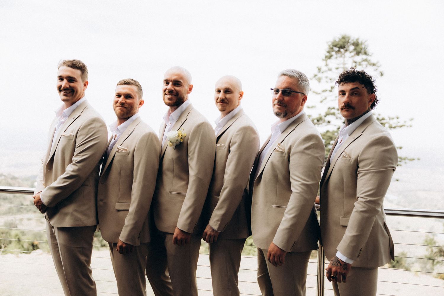 Wedding party in beige suits standing in line outdoors.