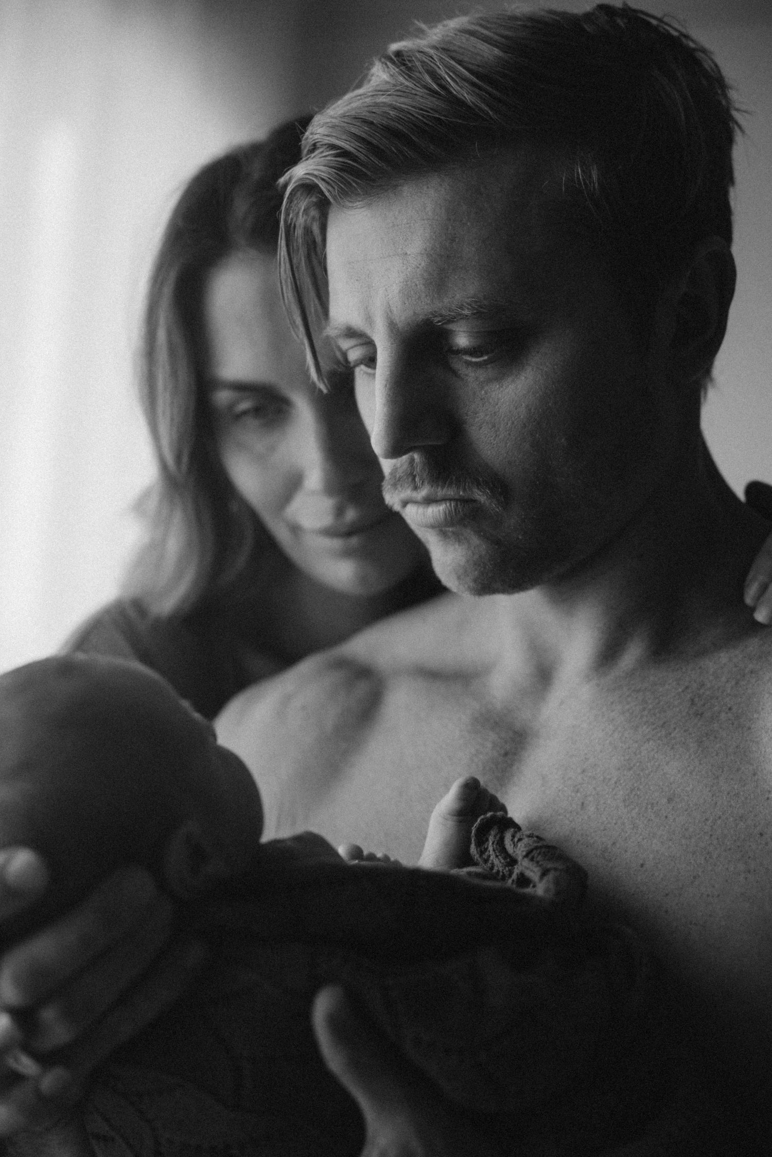 Black and white portrait of couple sharing tender moment with sleeping newborn.