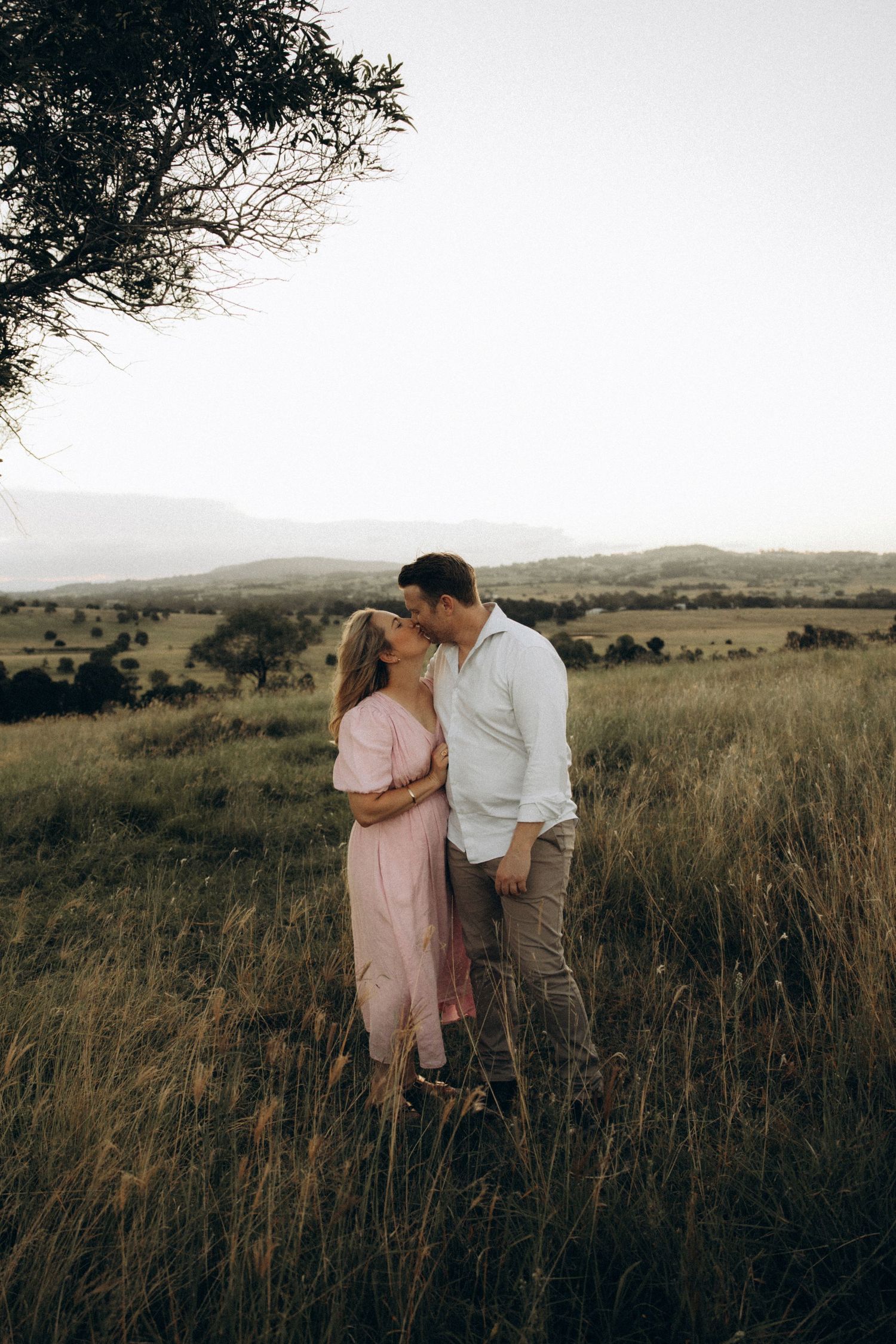 A couple shares an intimate moment in a serene field at dusk.