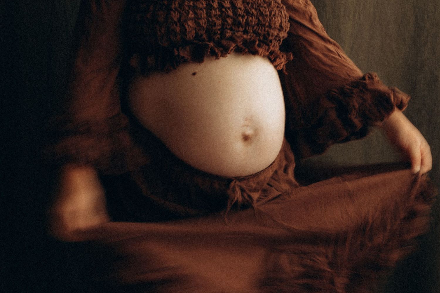 Pregnant woman in brown dress and knit hat showcasing baby bump in artistic maternity photography.