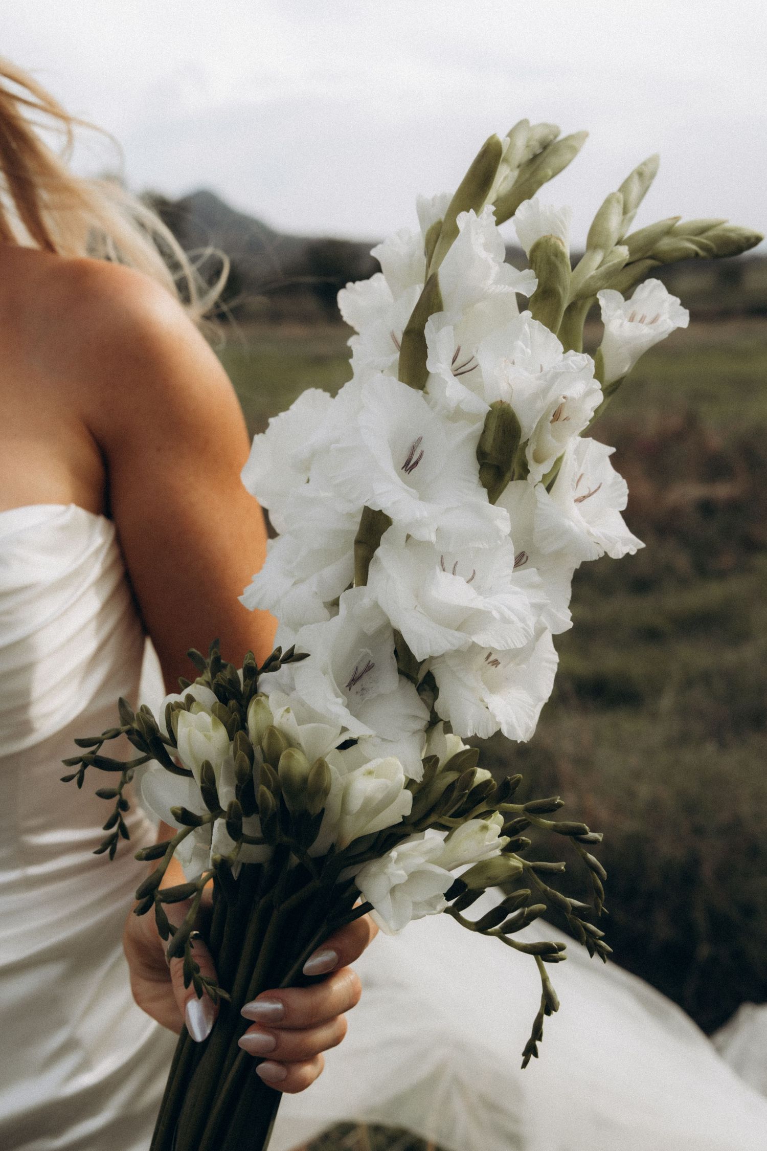 Close-up of white gladiolus flowers in a bridal bouquet against a white dress.