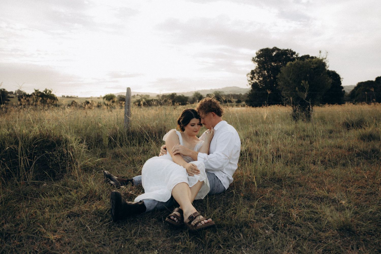 Couple lying together in a grassy field during golden hour.