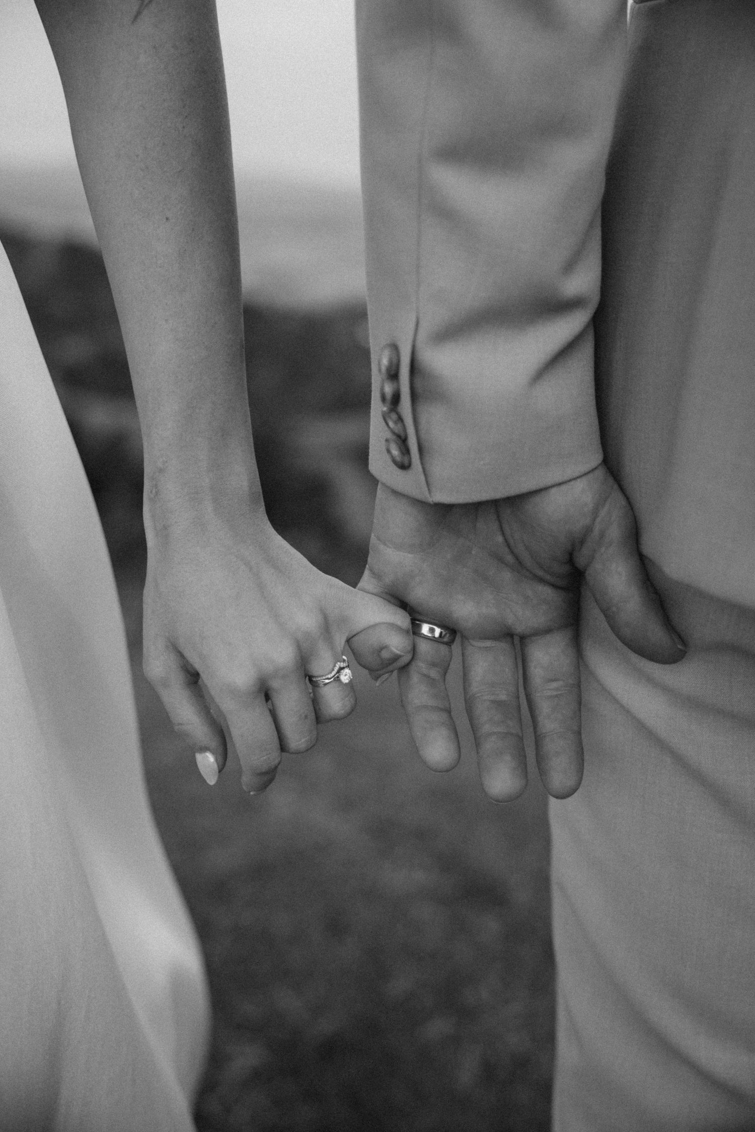 Black and white close-up of newlyweds holding hands, showing wedding rings.