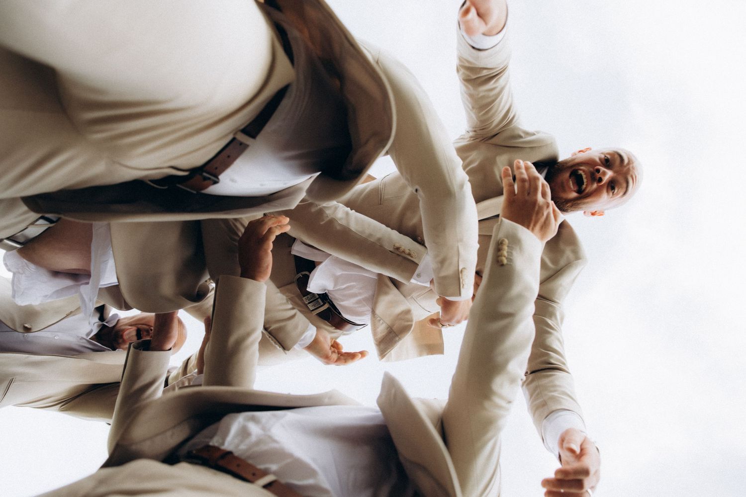 Groomsmen in beige suits pose playfully for a group photo.