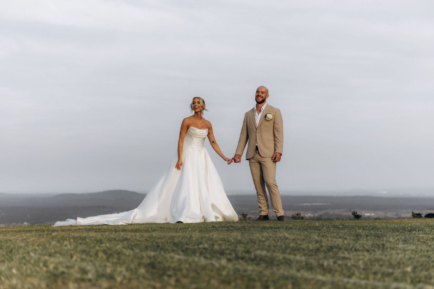 Wedding couple standing together on a scenic hilltop overlooking distant mountains.