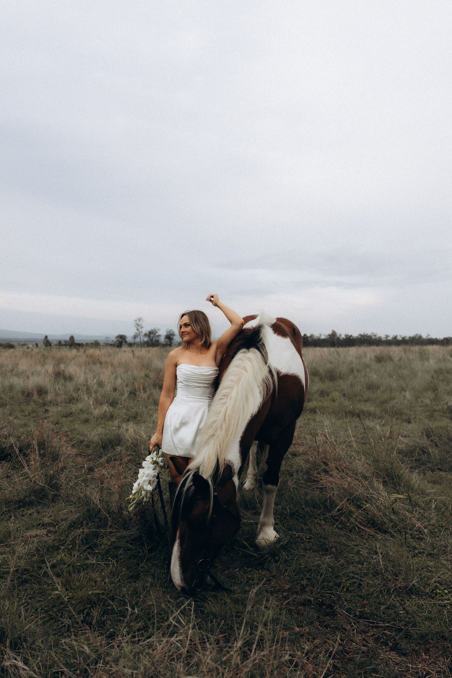 A couple embraces near a horse in a moody countryside setting.