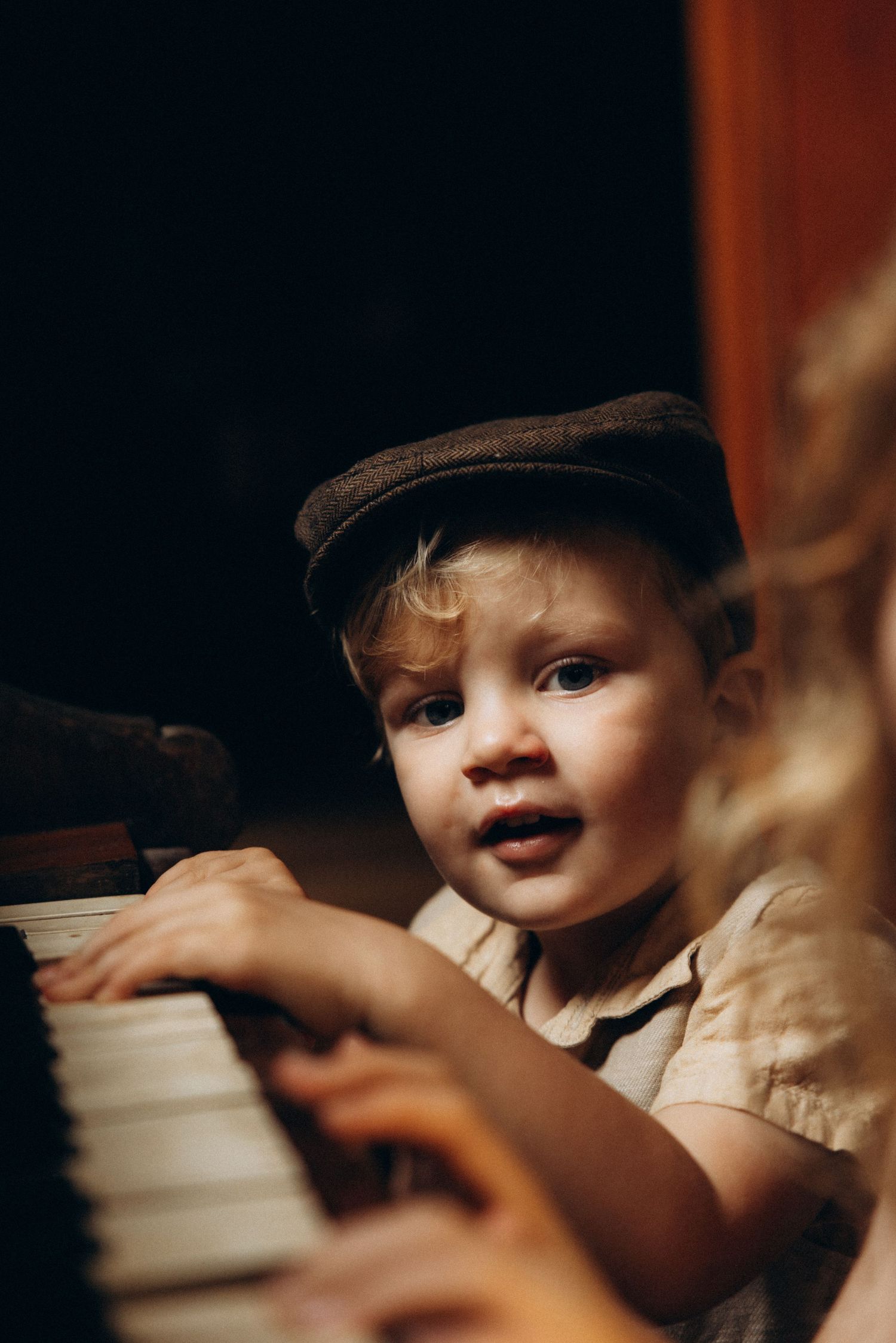 Young child in a cap reaching towards a white cup in dramatic lighting.
