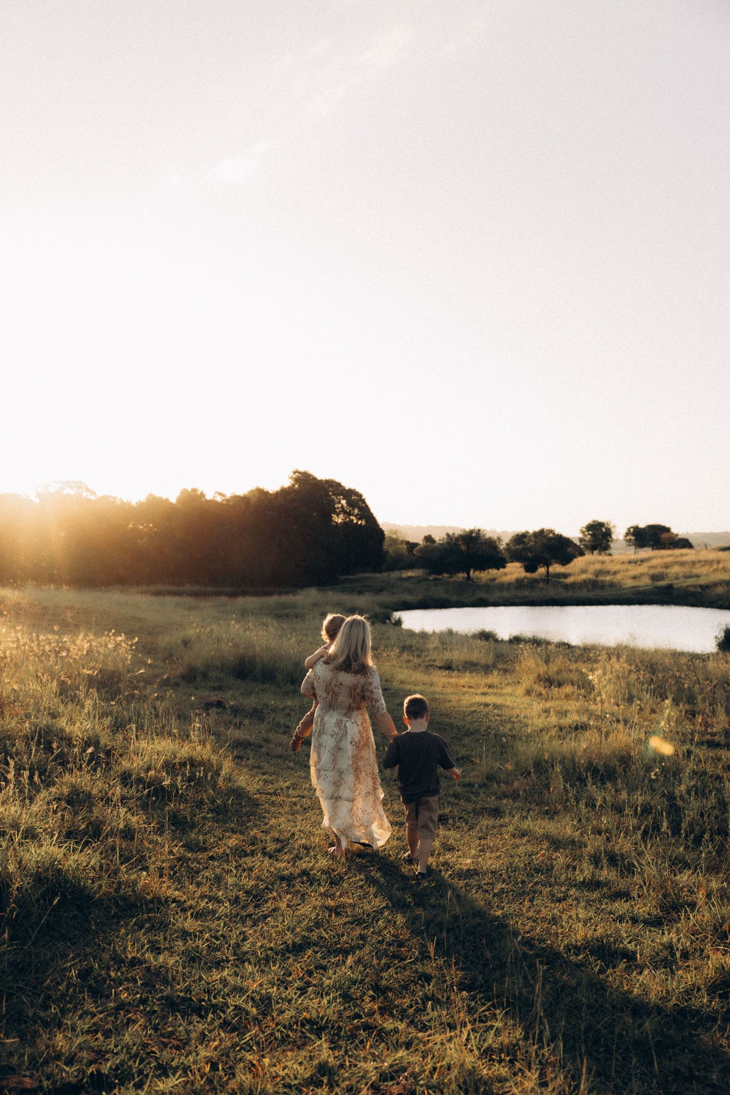 Bride in white dress walks through a sunlit field at golden hour.