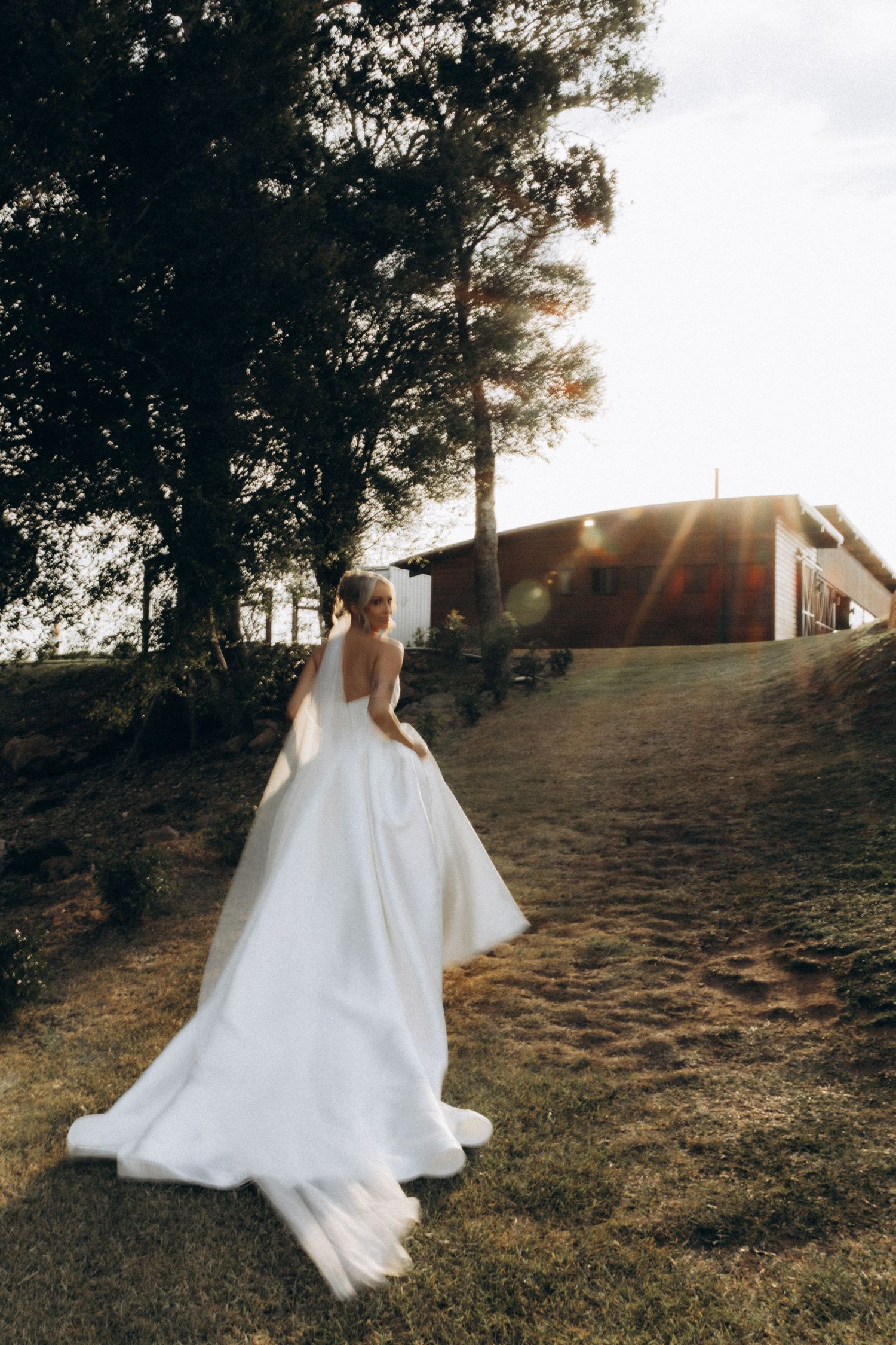 Flowing white wedding dress billowing in the breeze against a hillside backdrop at golden hour.