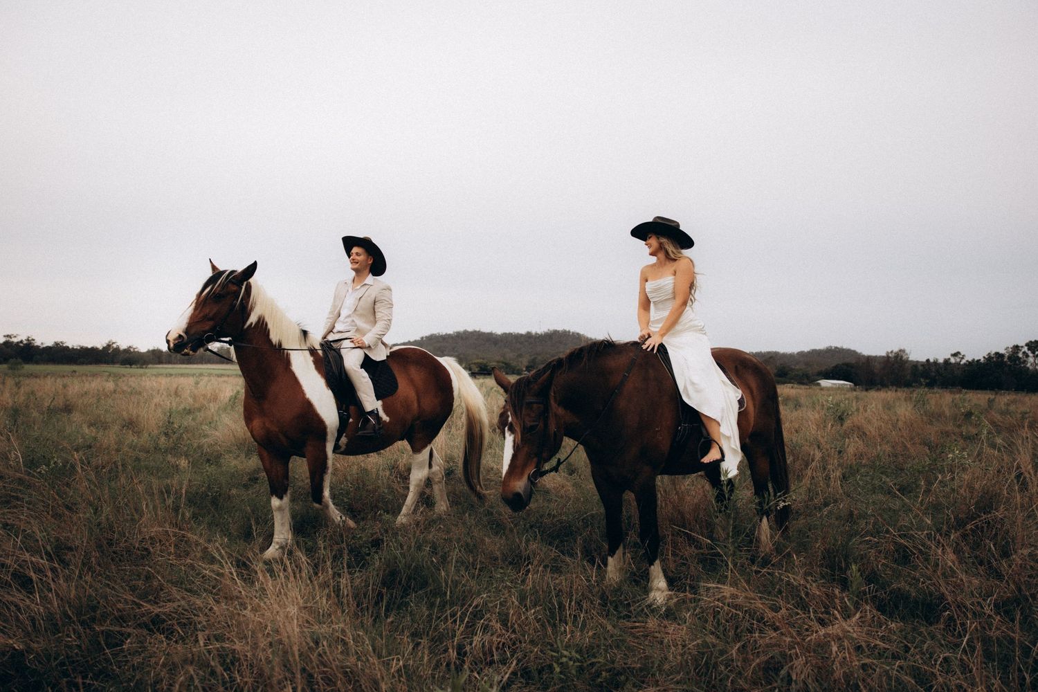 Scenic countryside photo with horses and riders against an overcast sky.