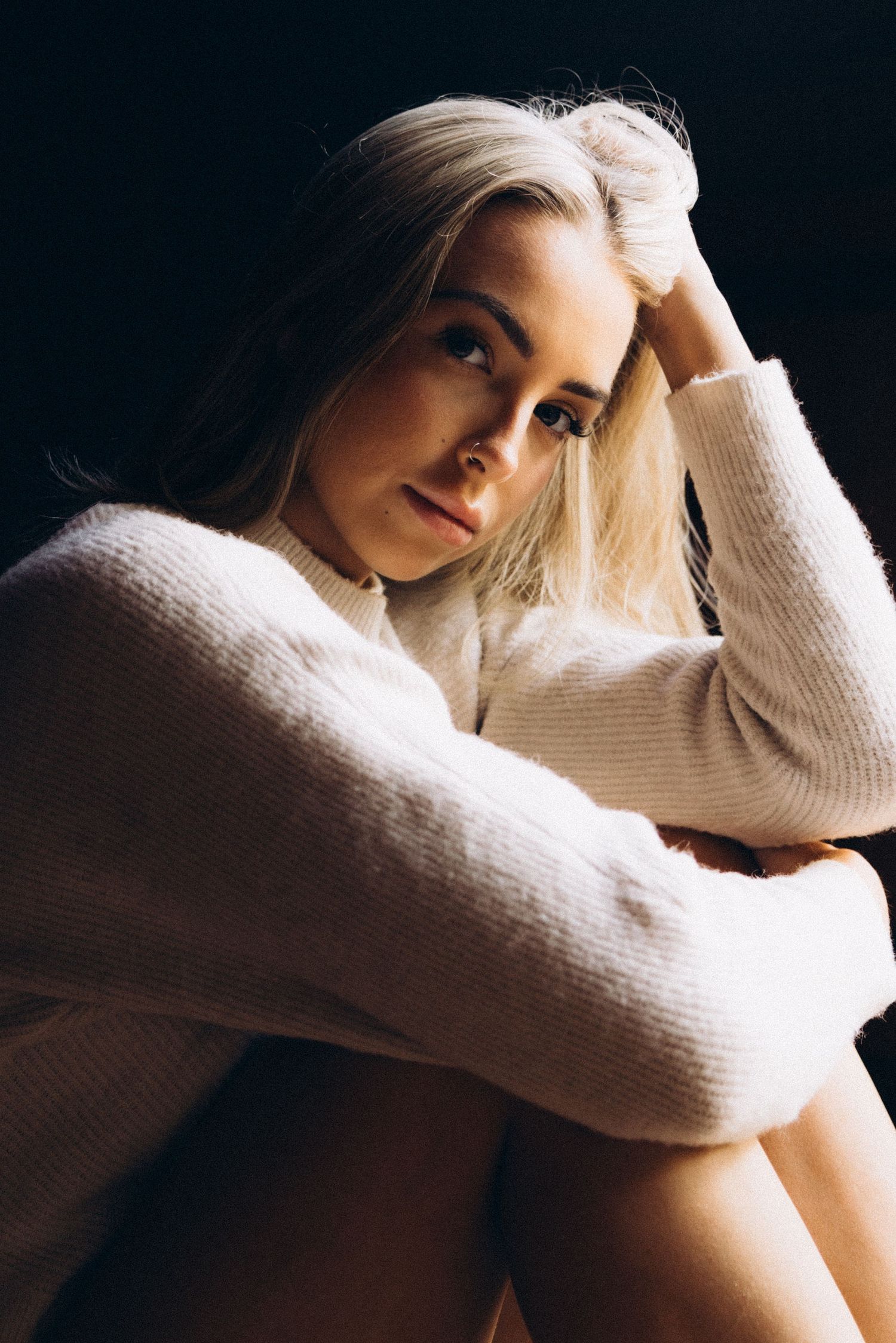 Intimate portrait in cream sweater with natural window lighting.