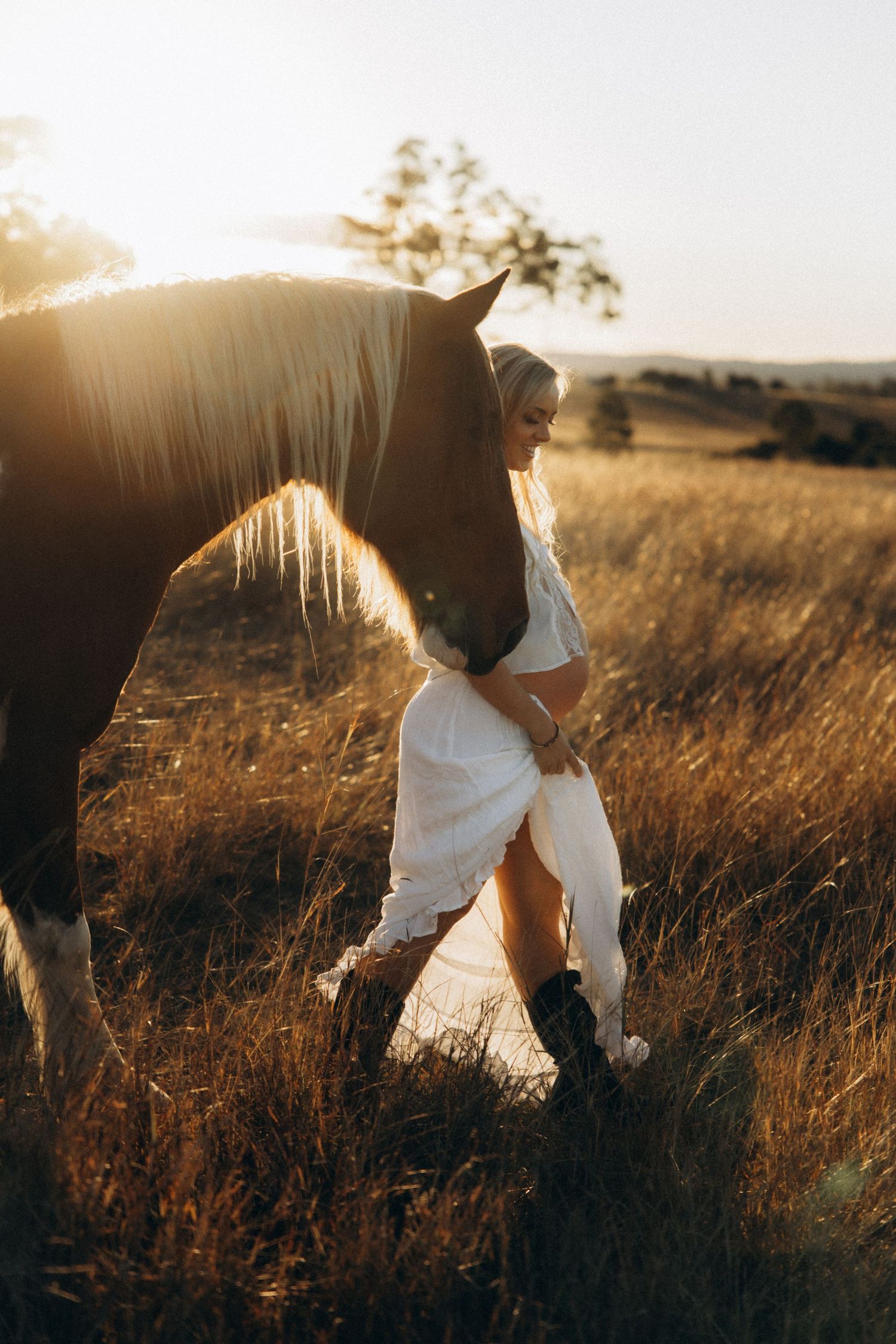 Woman in white dress embracing a palomino horse in golden field at sunset.