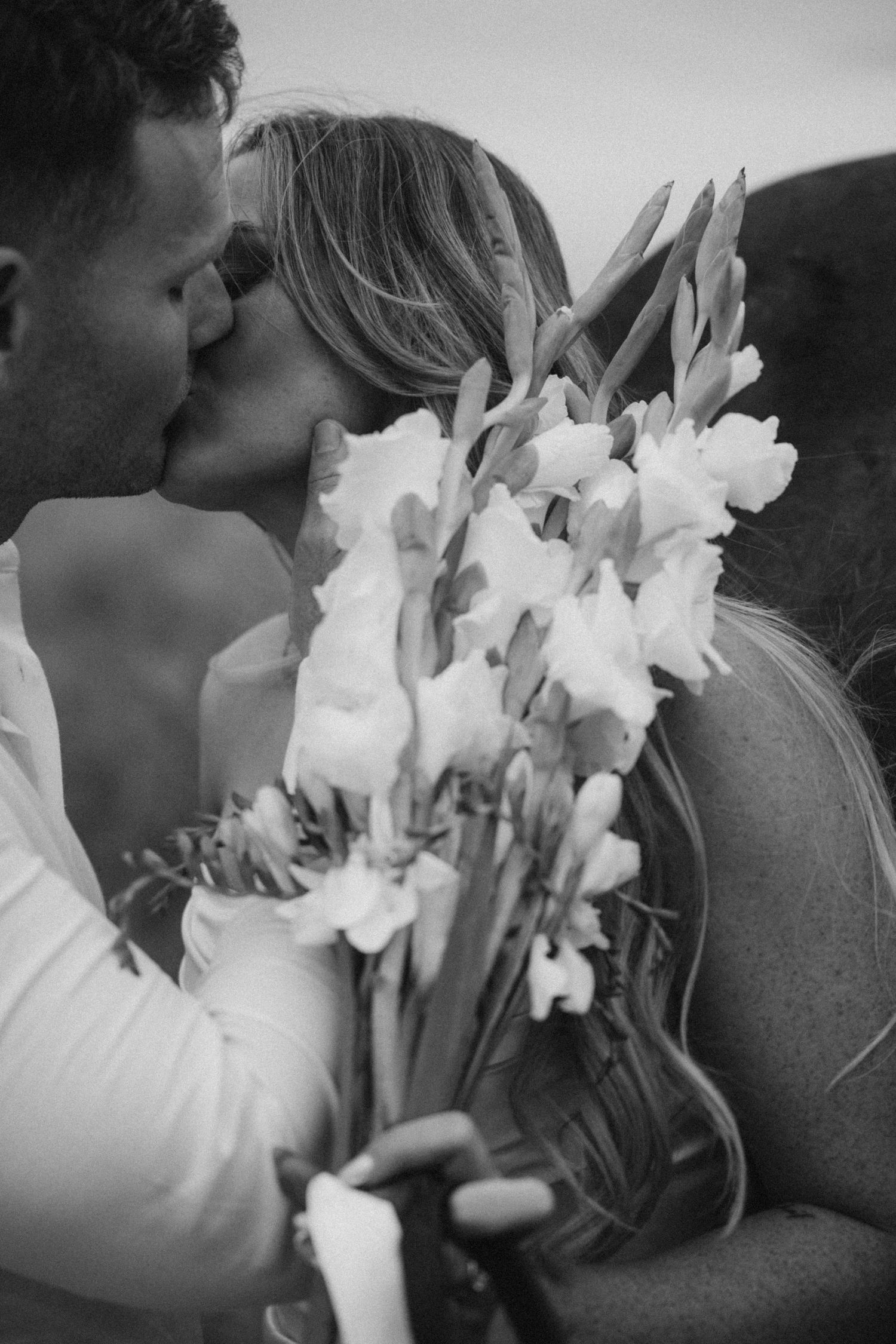 Wedding couple shares a kiss while holding white flowers.
