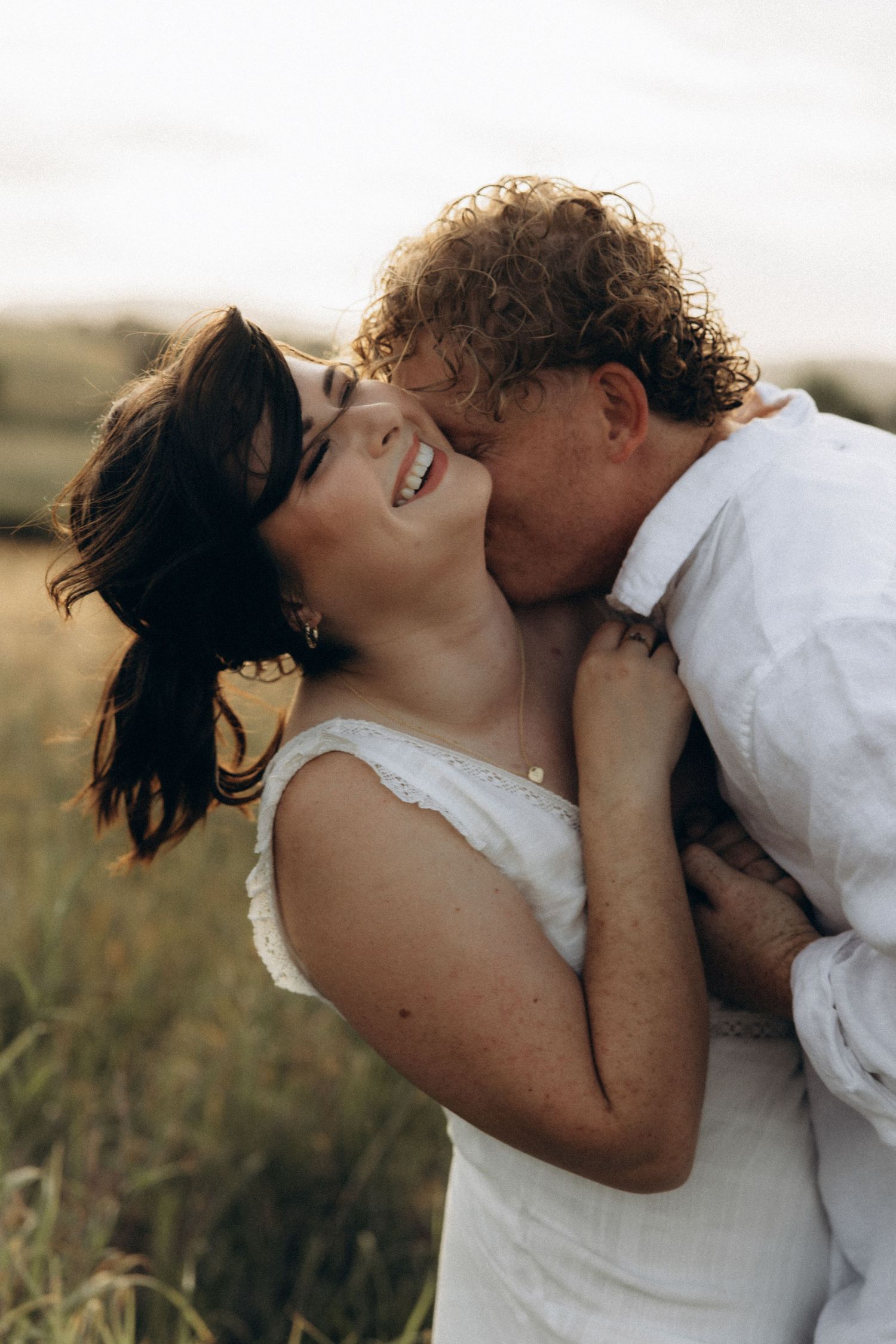 Couple shares intimate kiss in sunlit field during photo session.