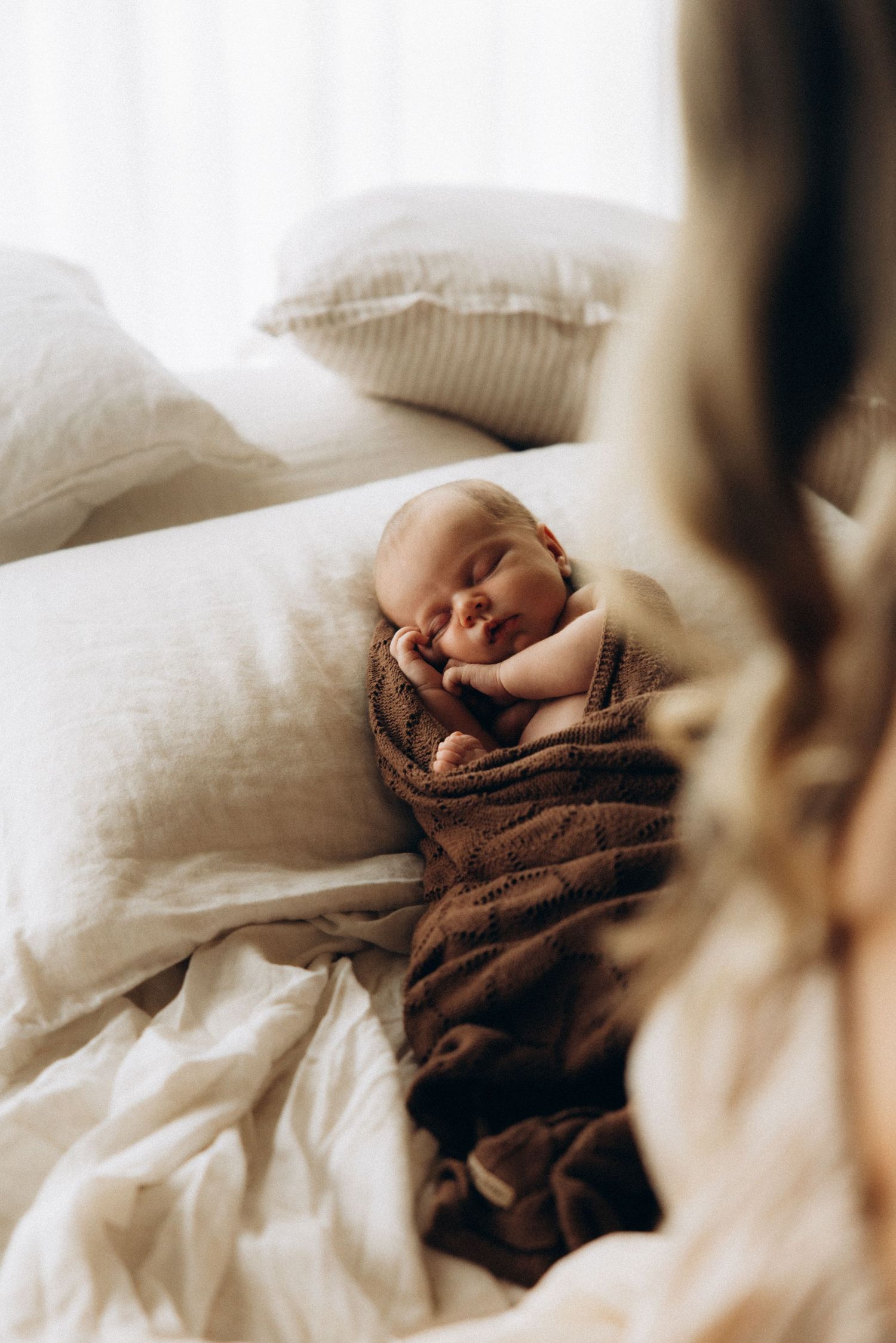Close-up view of someone wrapped in a brown blanket resting on white pillows.