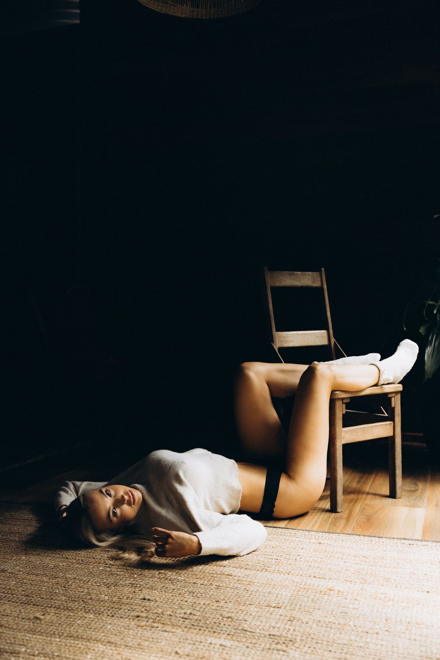 Minimalist boudoir photography with dramatic shadows on wooden floor.
