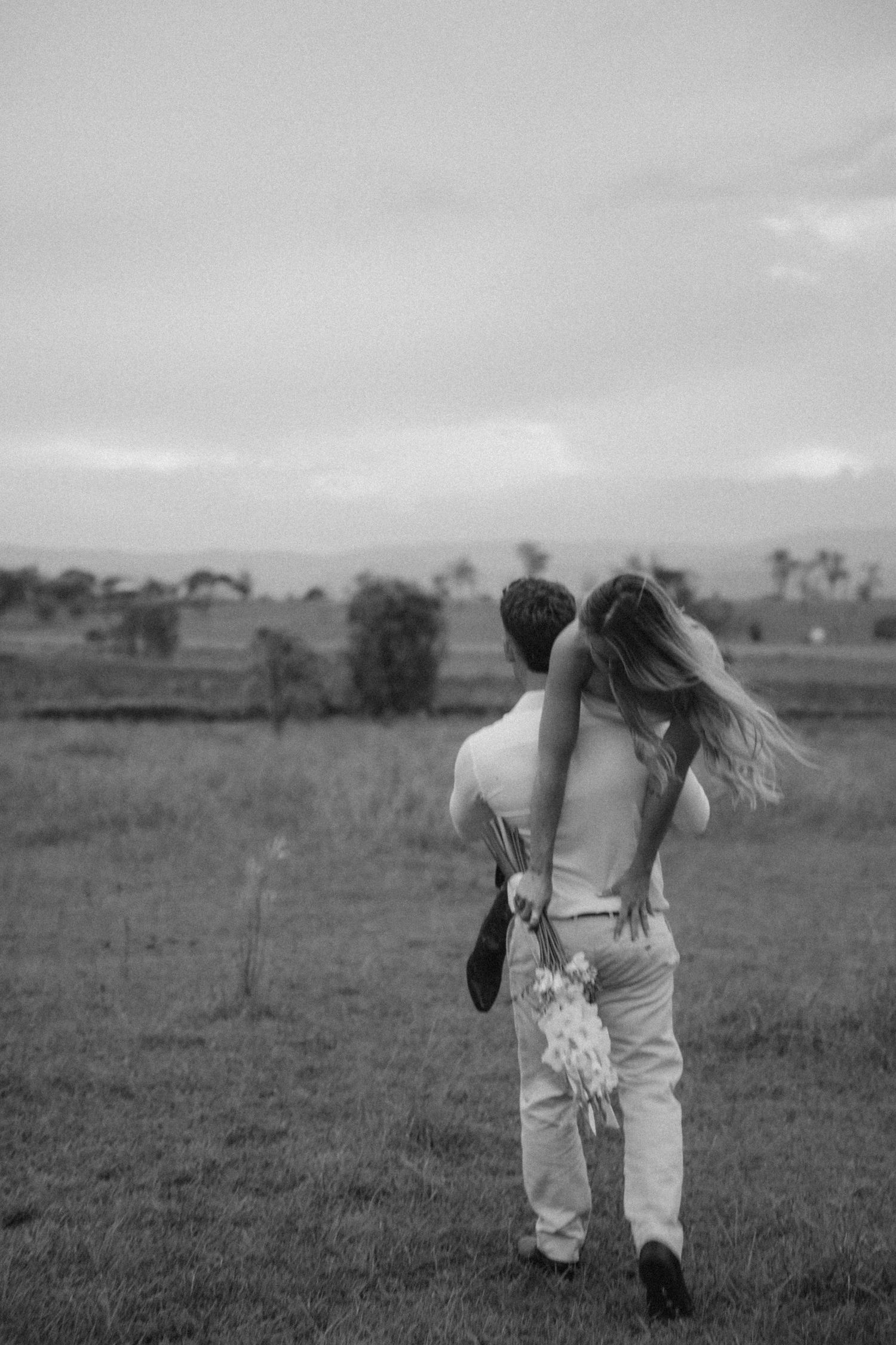 Two people in white outfits dancing together in a rustic field setting.