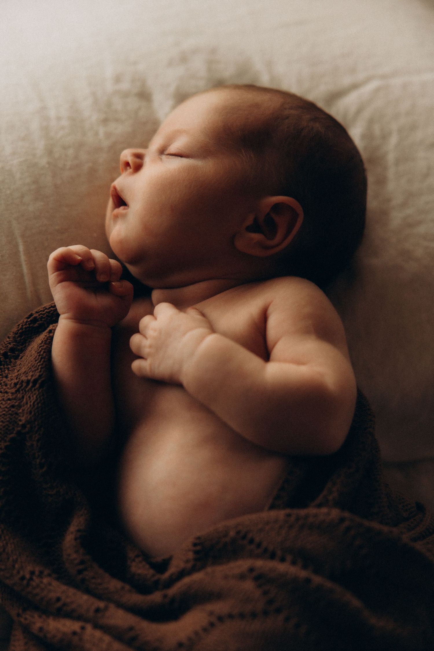 Artistic photographs of a sleeping baby wrapped in a brown blanket.