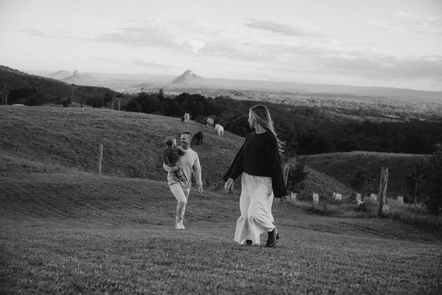 Two women walk across a lush green hillside at dusk with a mountain landscape in the background.