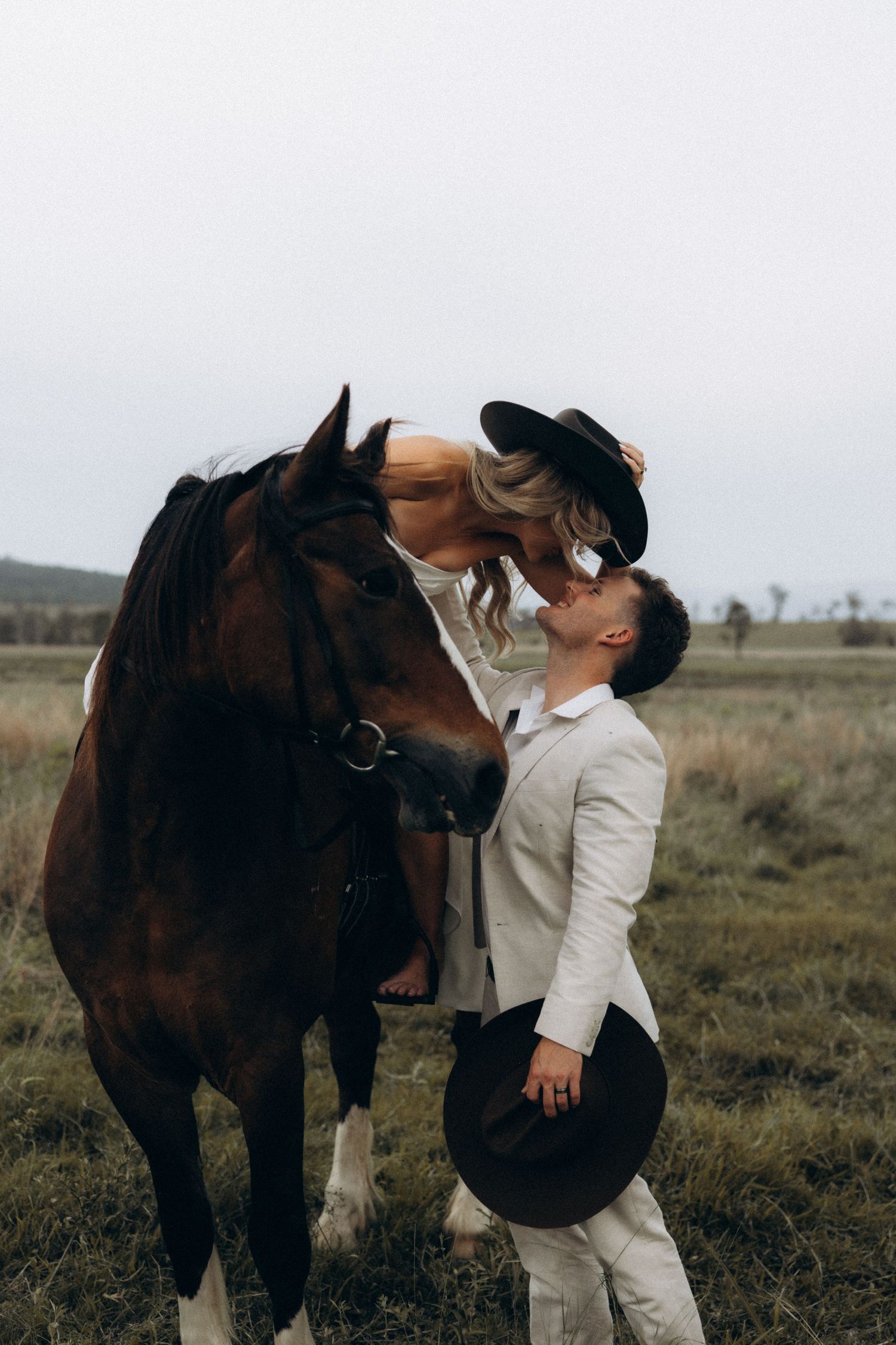 A person in white clothing interacts affectionately with a large brown horse in a field.