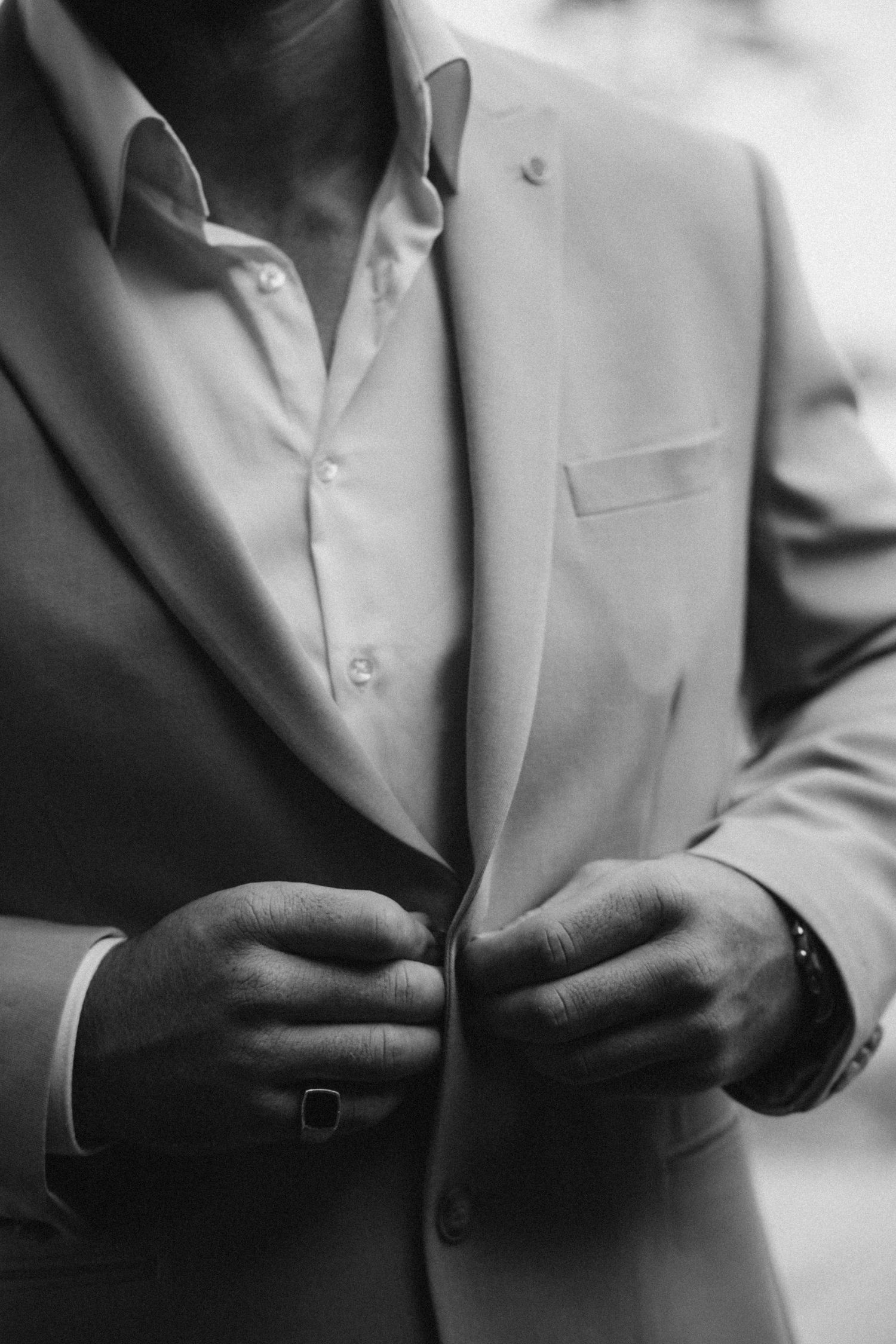 Close-up black and white shots of someone adjusting formal suit buttons.