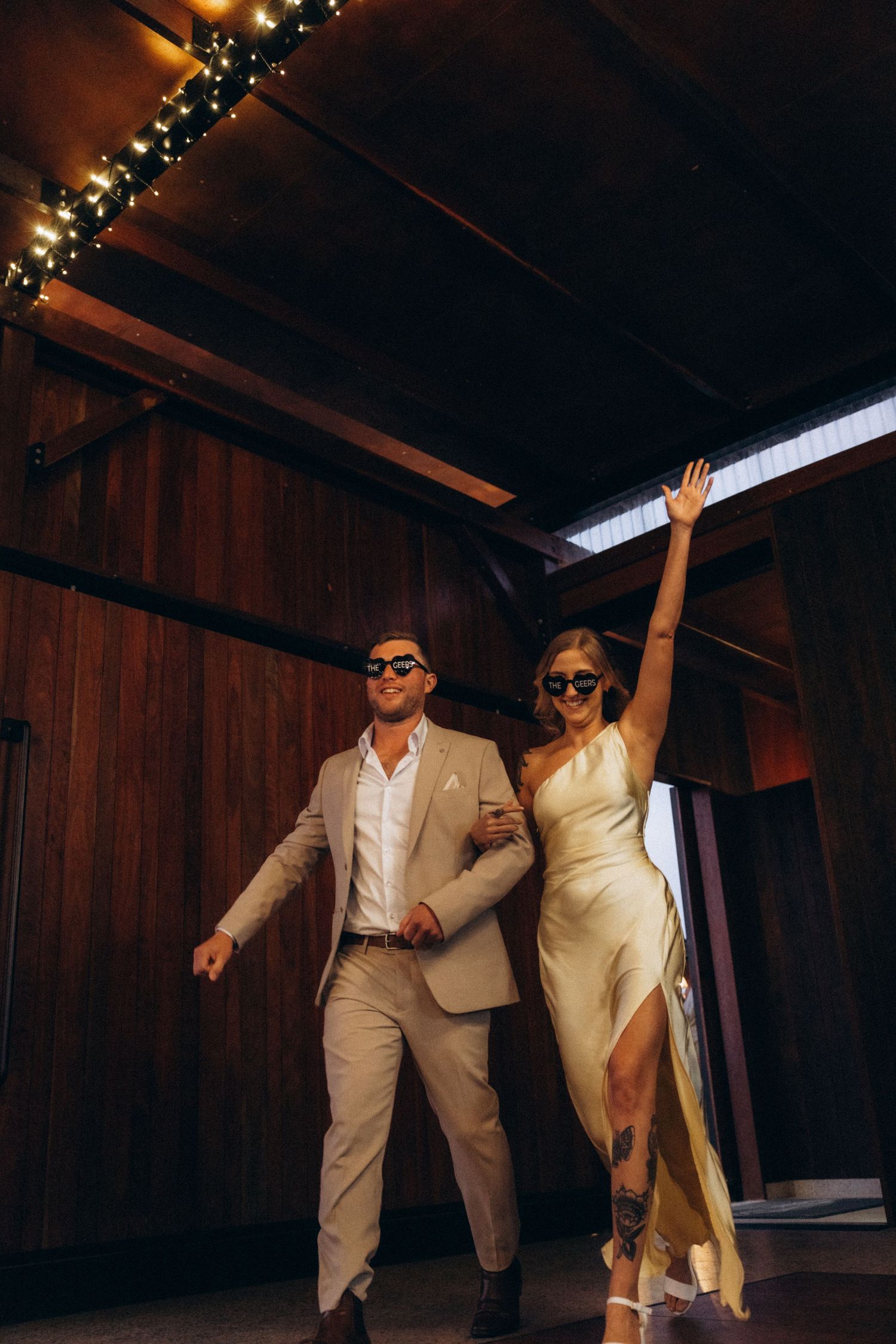 Wedding couple dances joyfully in a barn with twinkling lights overhead.