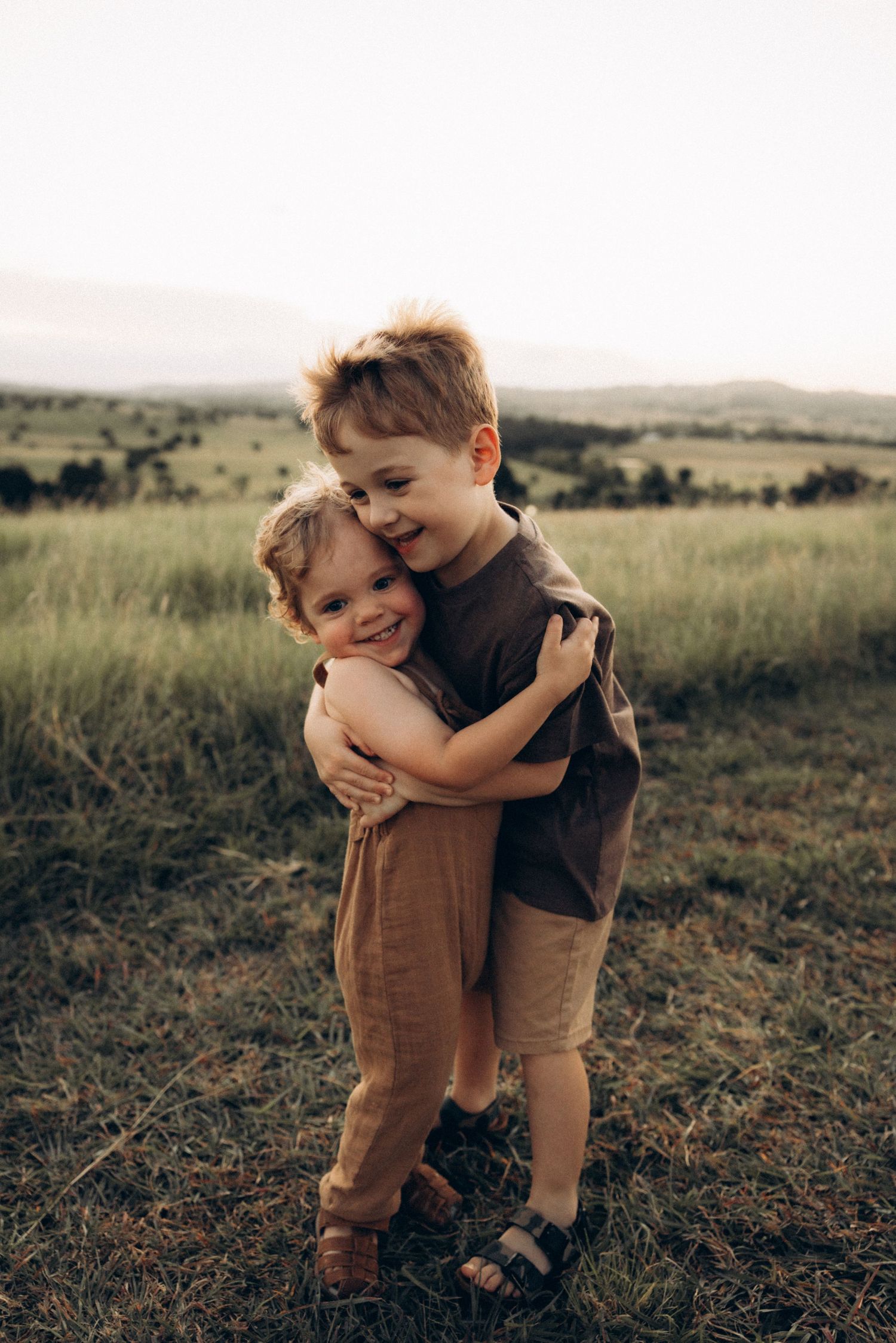 Two children share a warm hug while playing in a grassy field at sunset.