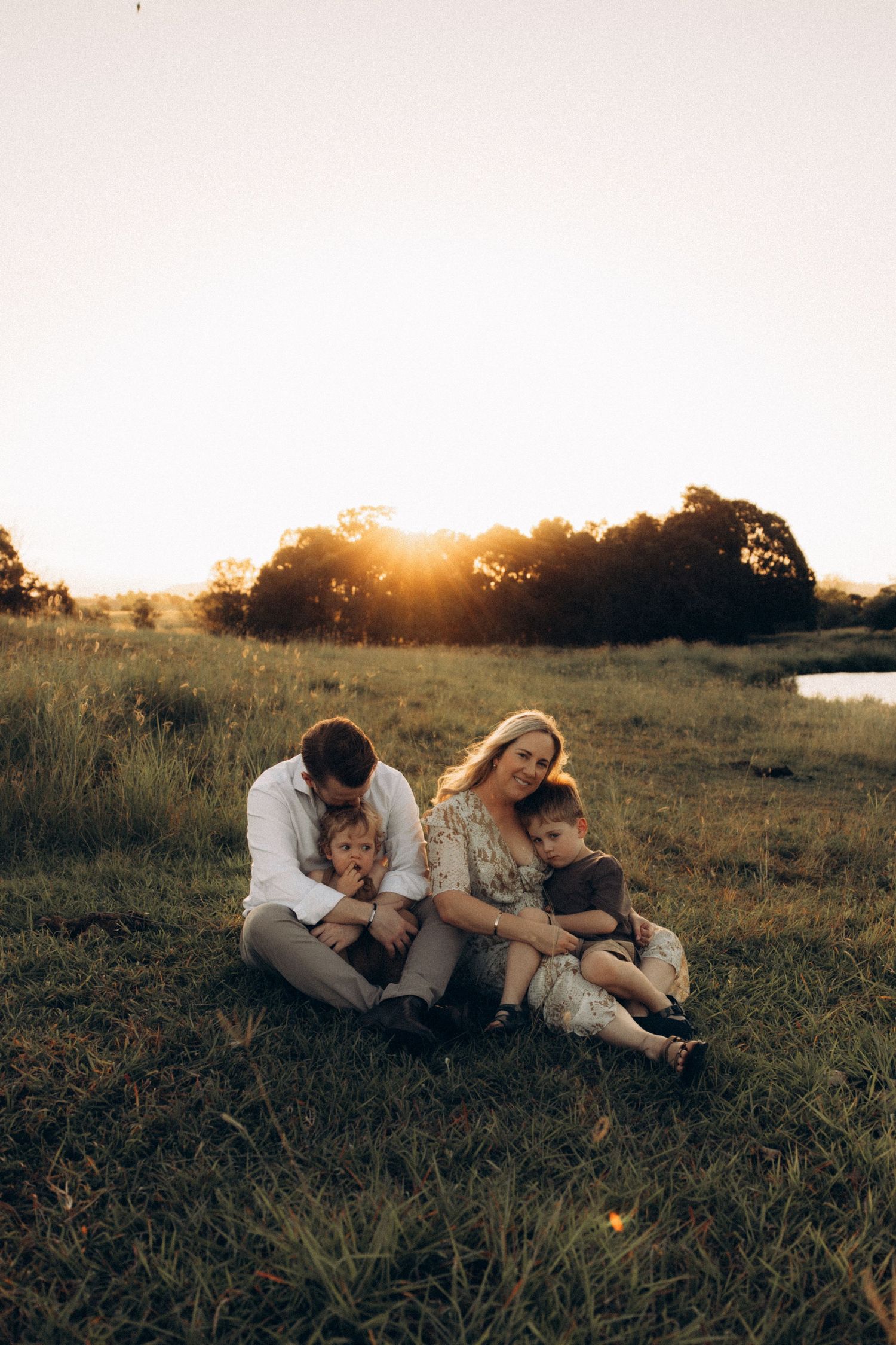 Family lying together on grass during sunset with water in background.