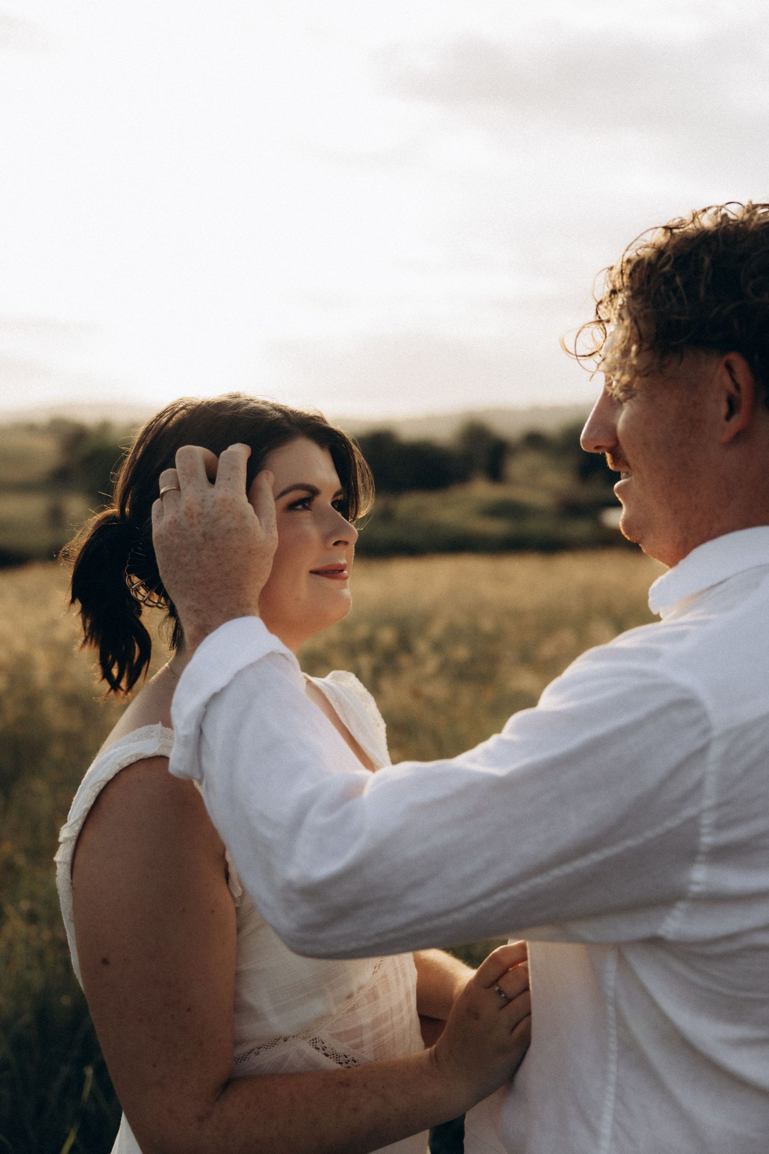 Intimate couple embraces in golden field during sunset photoshoot.
