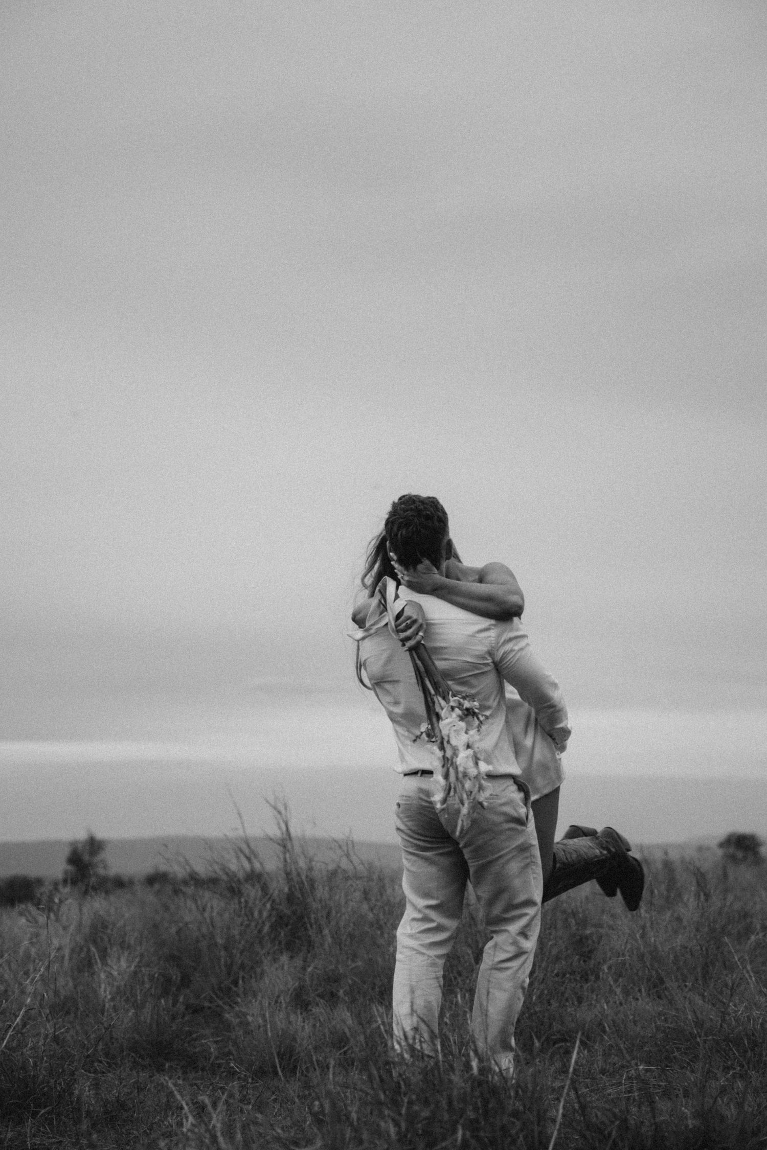 A couple walking through a grassy field in black and white.