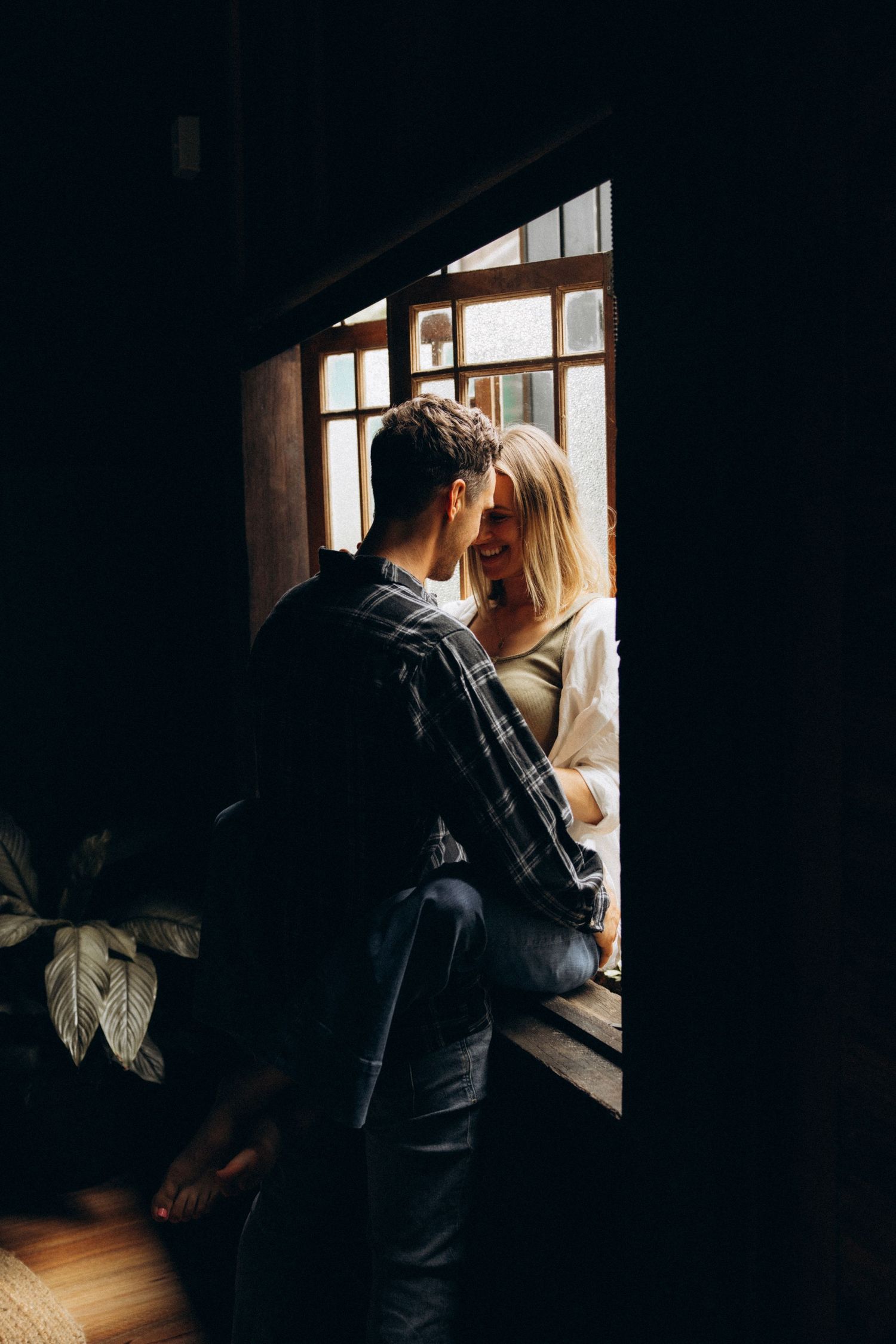 Intimate couple photos by a window with dramatic natural lighting and shadows.