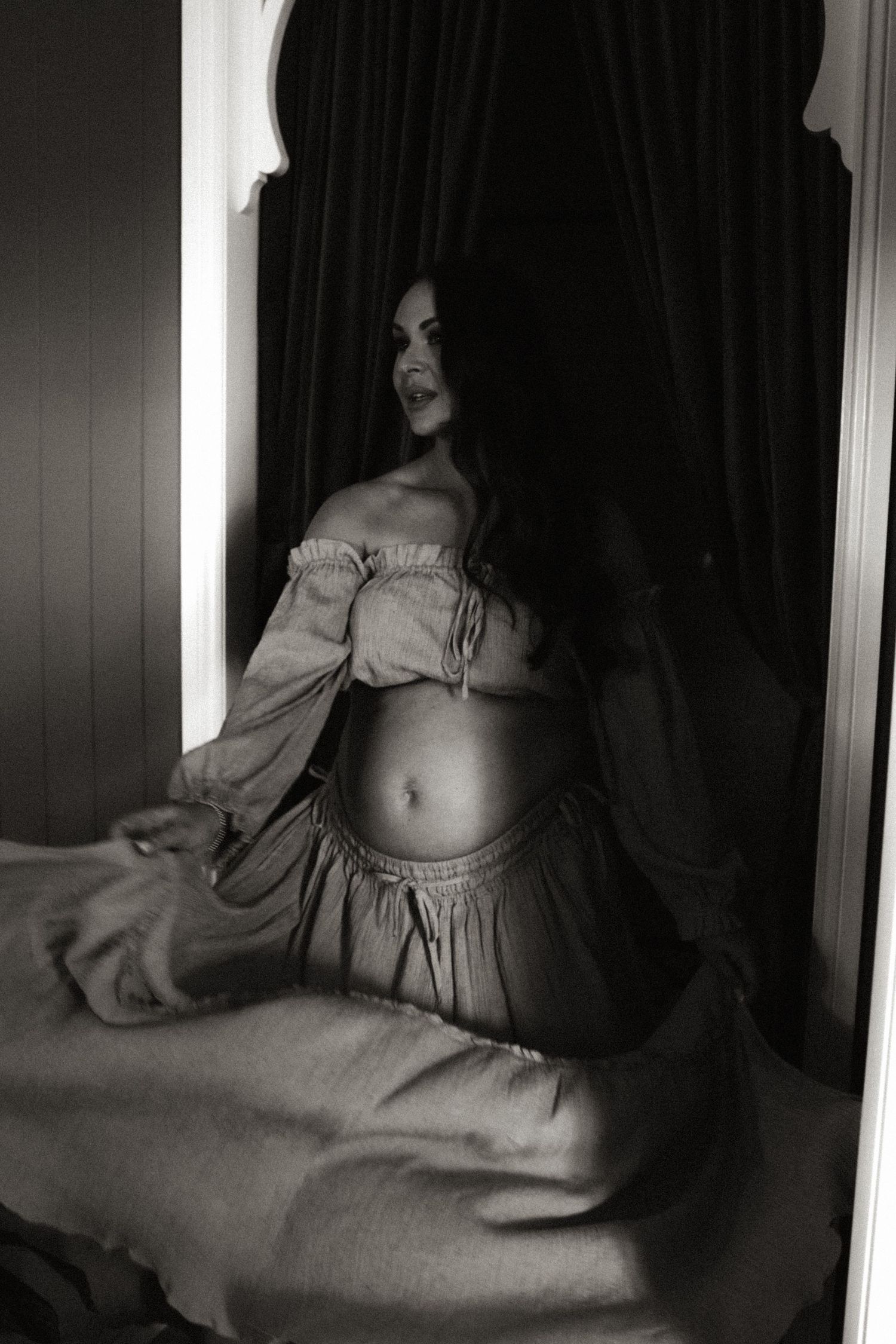 Artistic black and white boudoir photos showing a woman in flowing fabric against dark curtains.