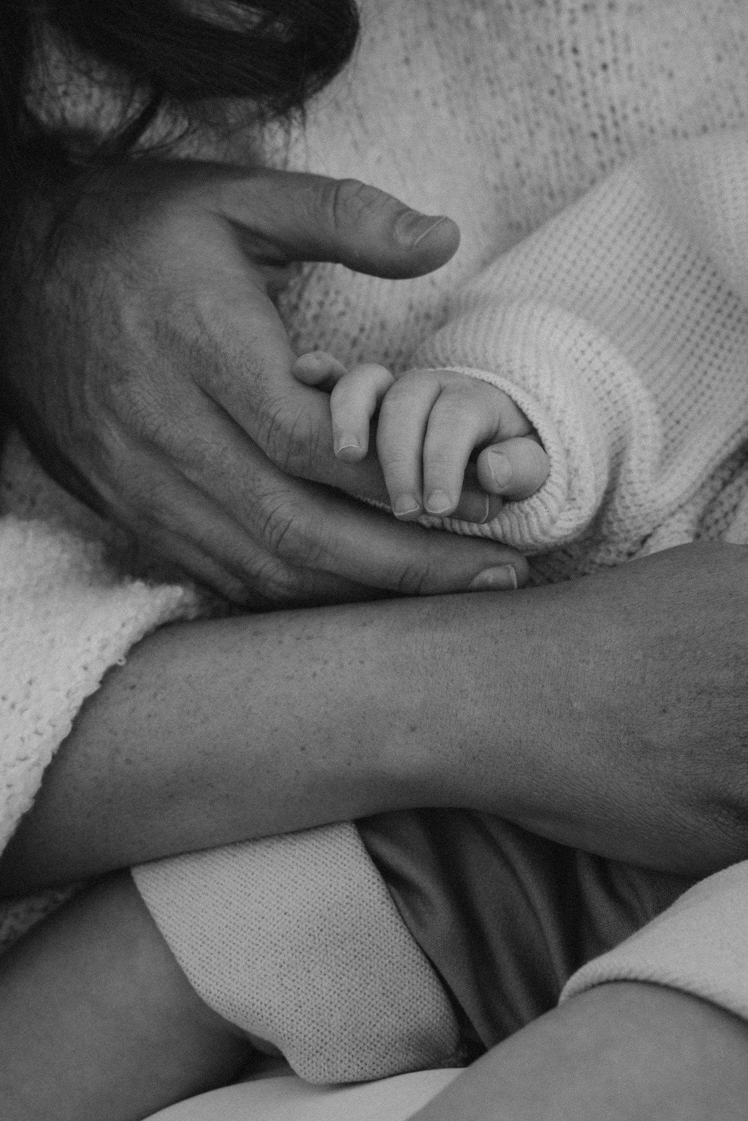 Black and white photo of a newborn baby grasping an adult's finger, symbolizing new life and parental bond.