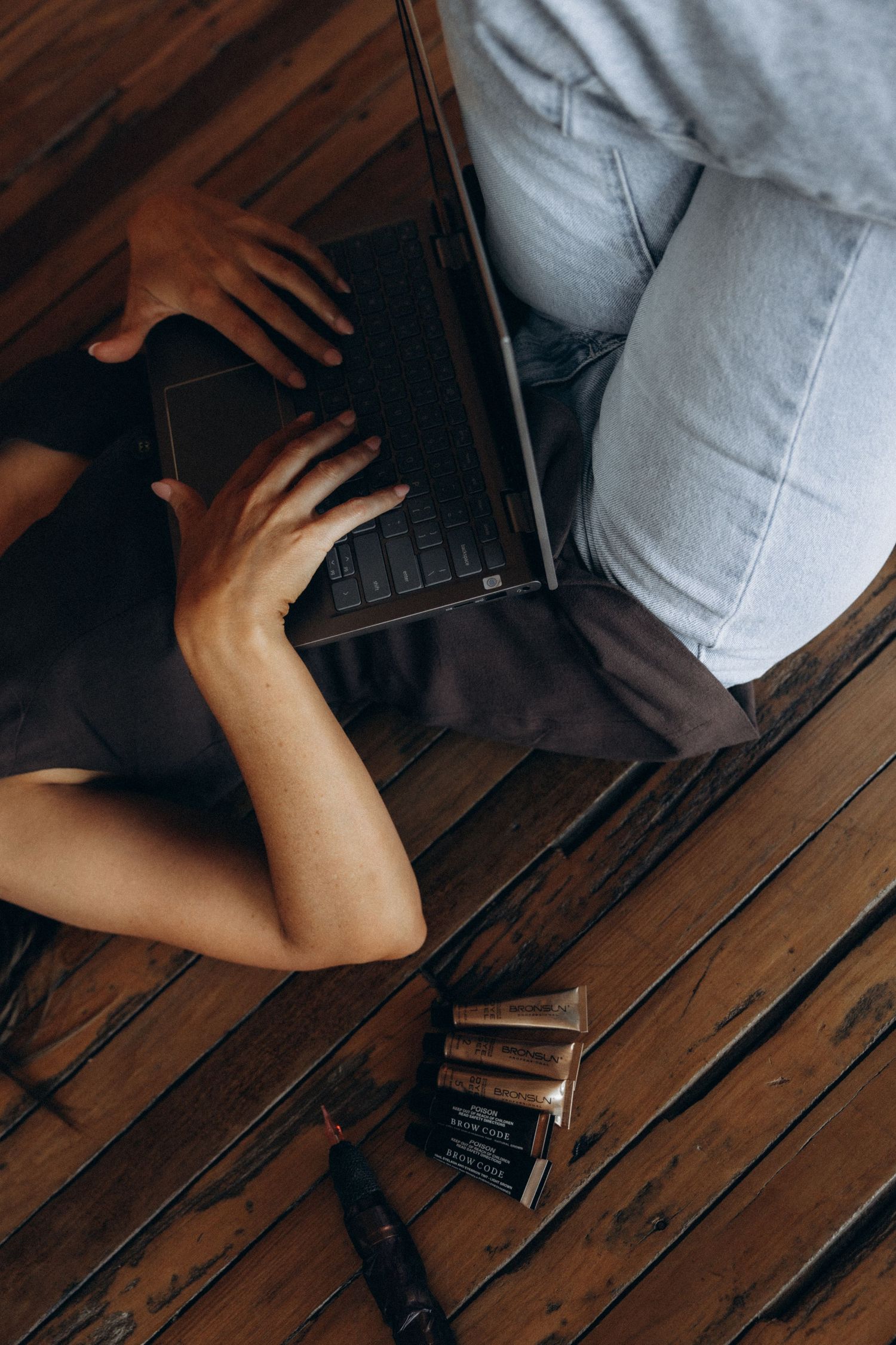 Overhead view of person working on laptop while lying on wooden floor.