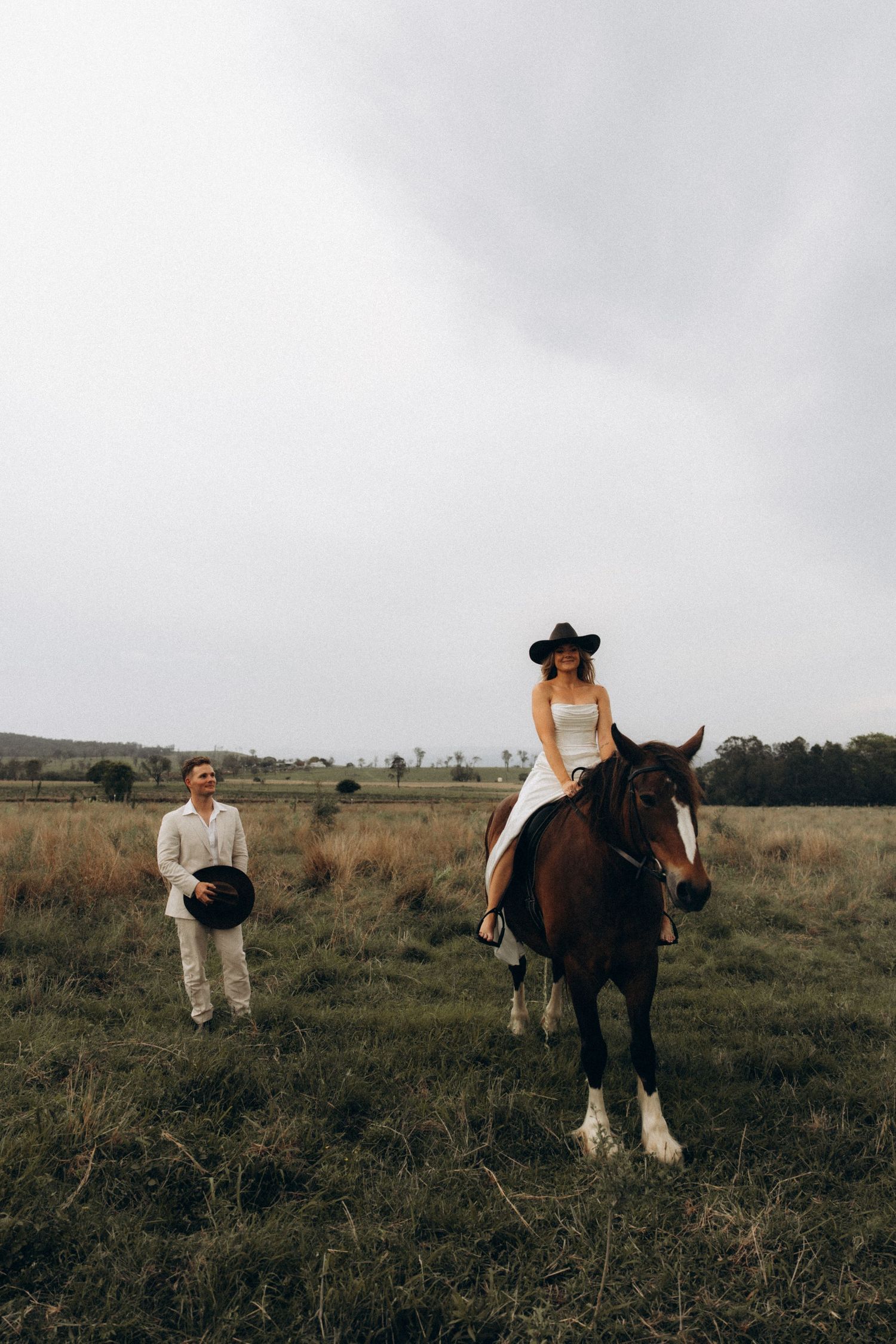 A couple poses with a majestic draft horse in a rustic field setting.