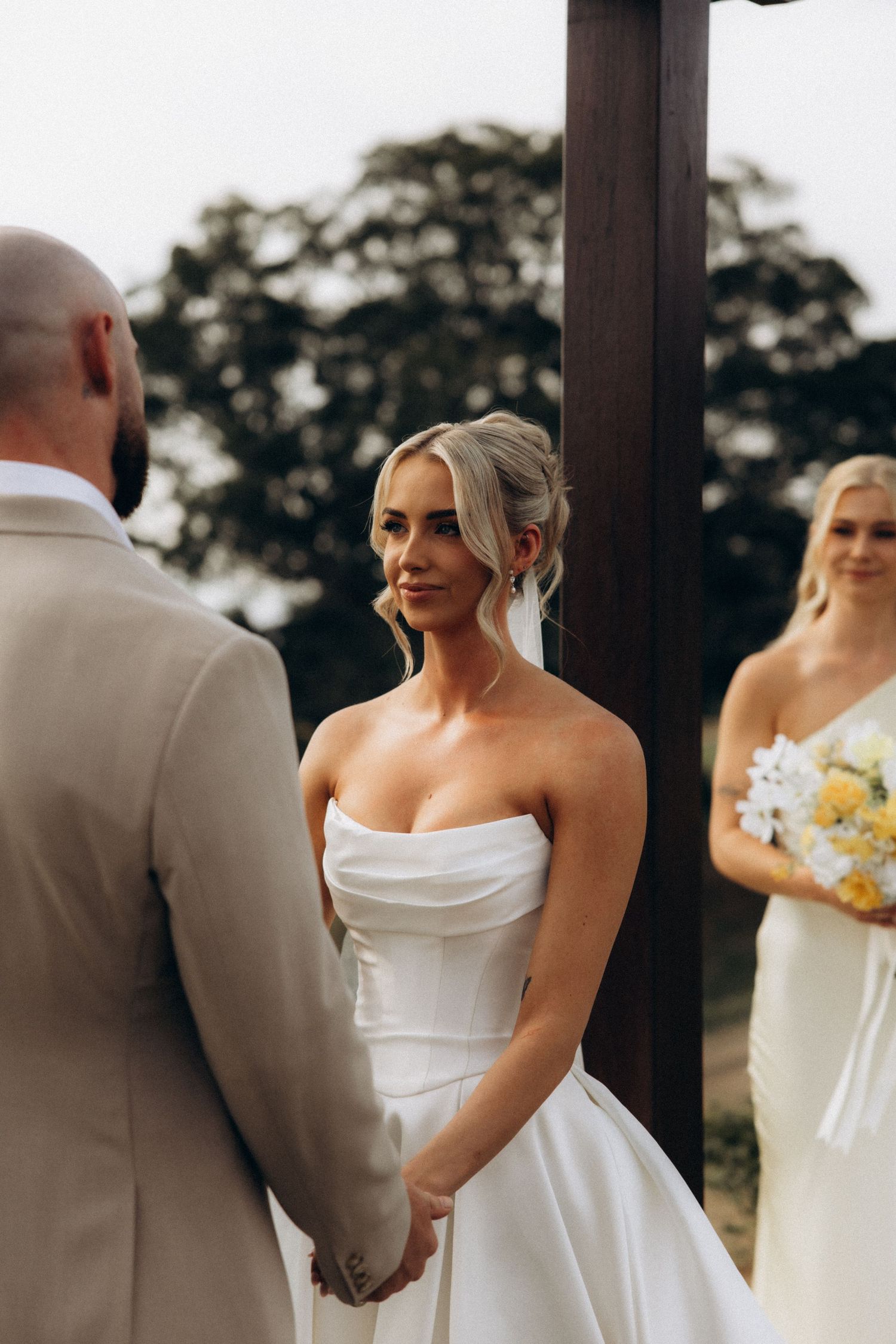 Wedding party lined up outdoors wearing white dresses and beige suits.