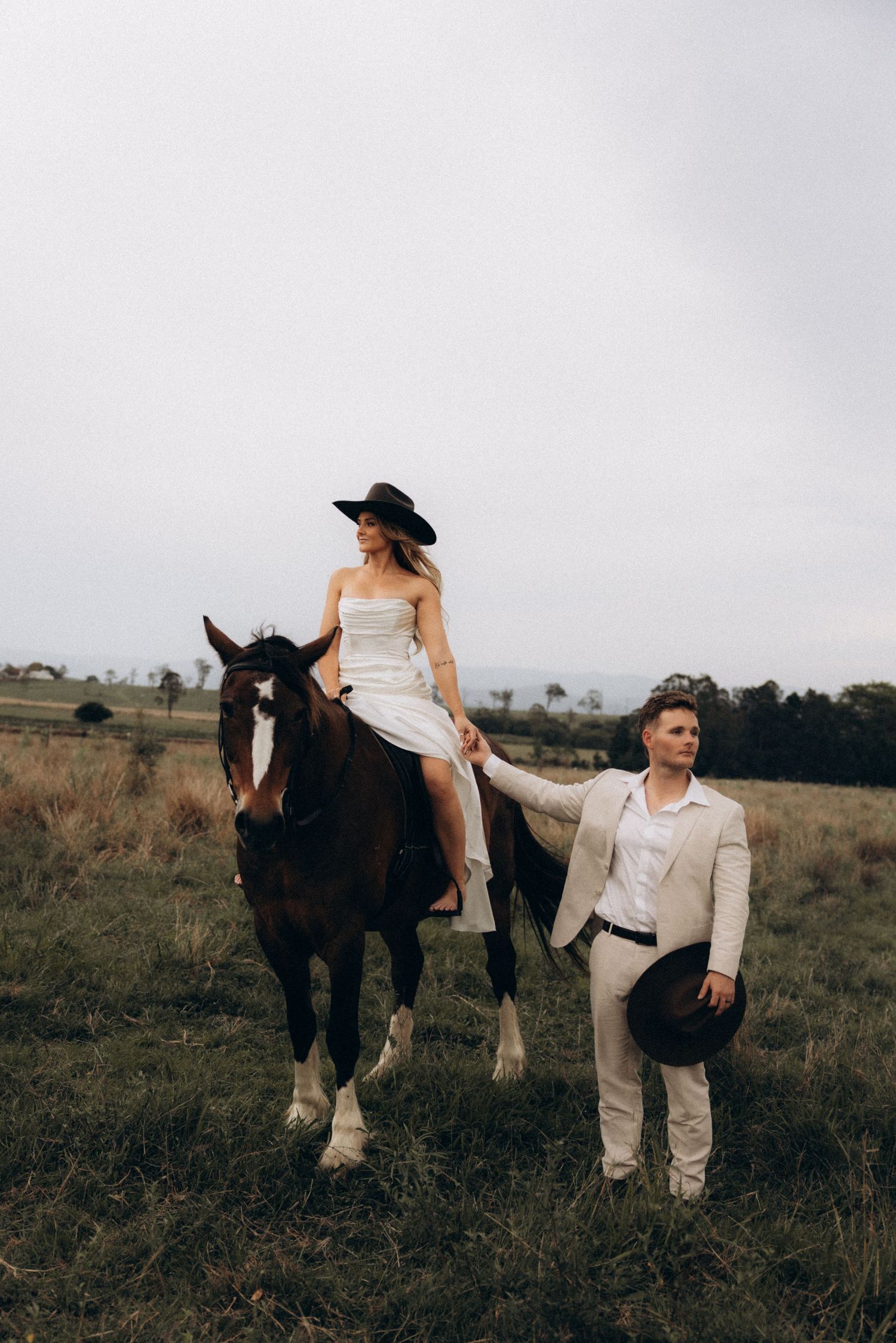 Couple posing with horses in a rustic field setting.