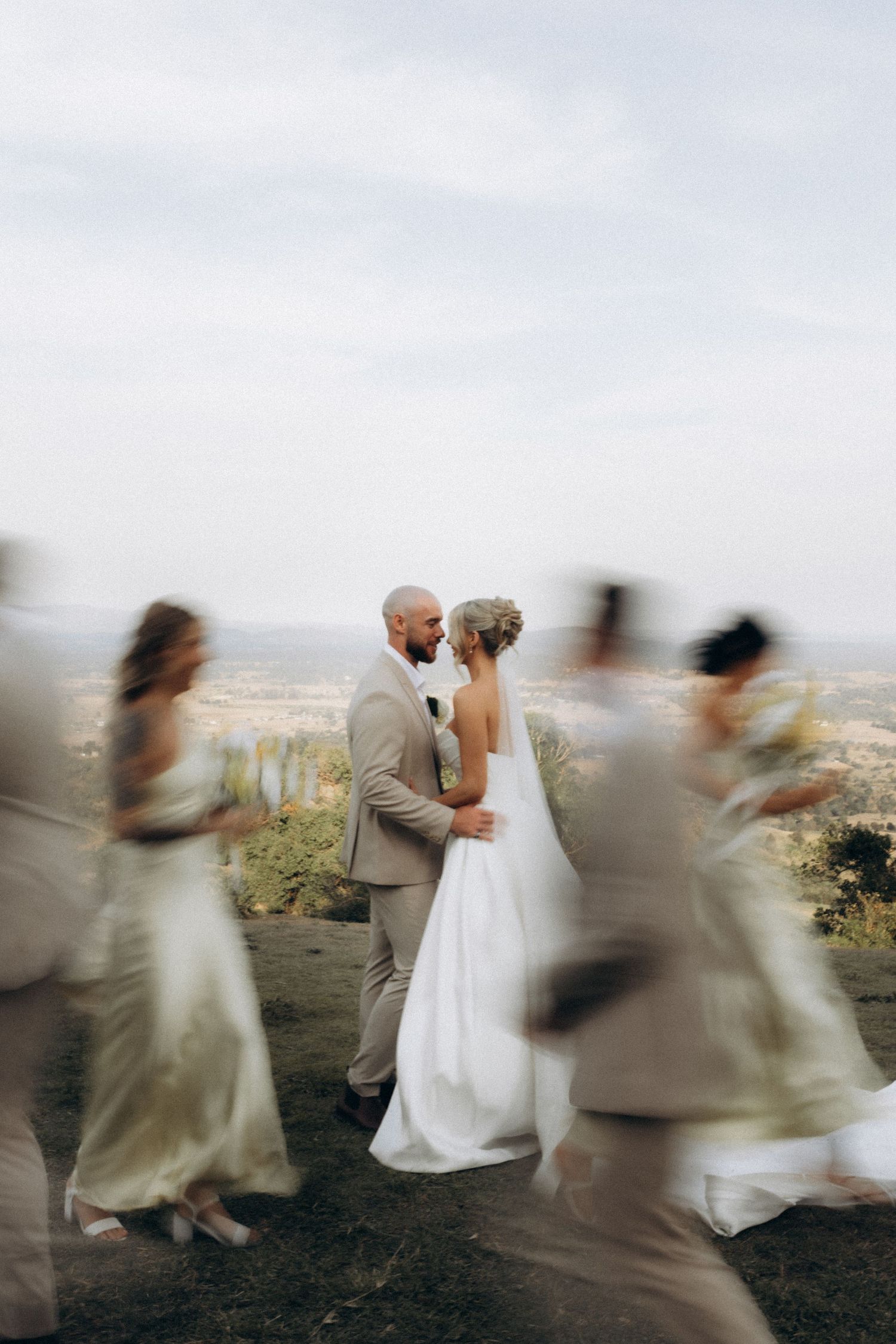 Artistic motion blur captures wedding party dancing around the newlyweds on a hilltop.